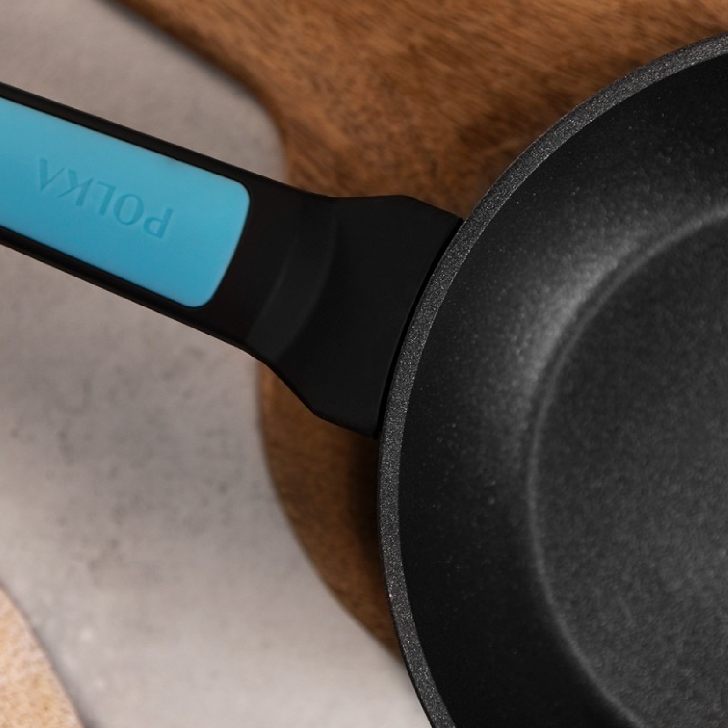 Zbliżenie czarnej patelni z niebieskim uchwytem. Tekst: POLKA.