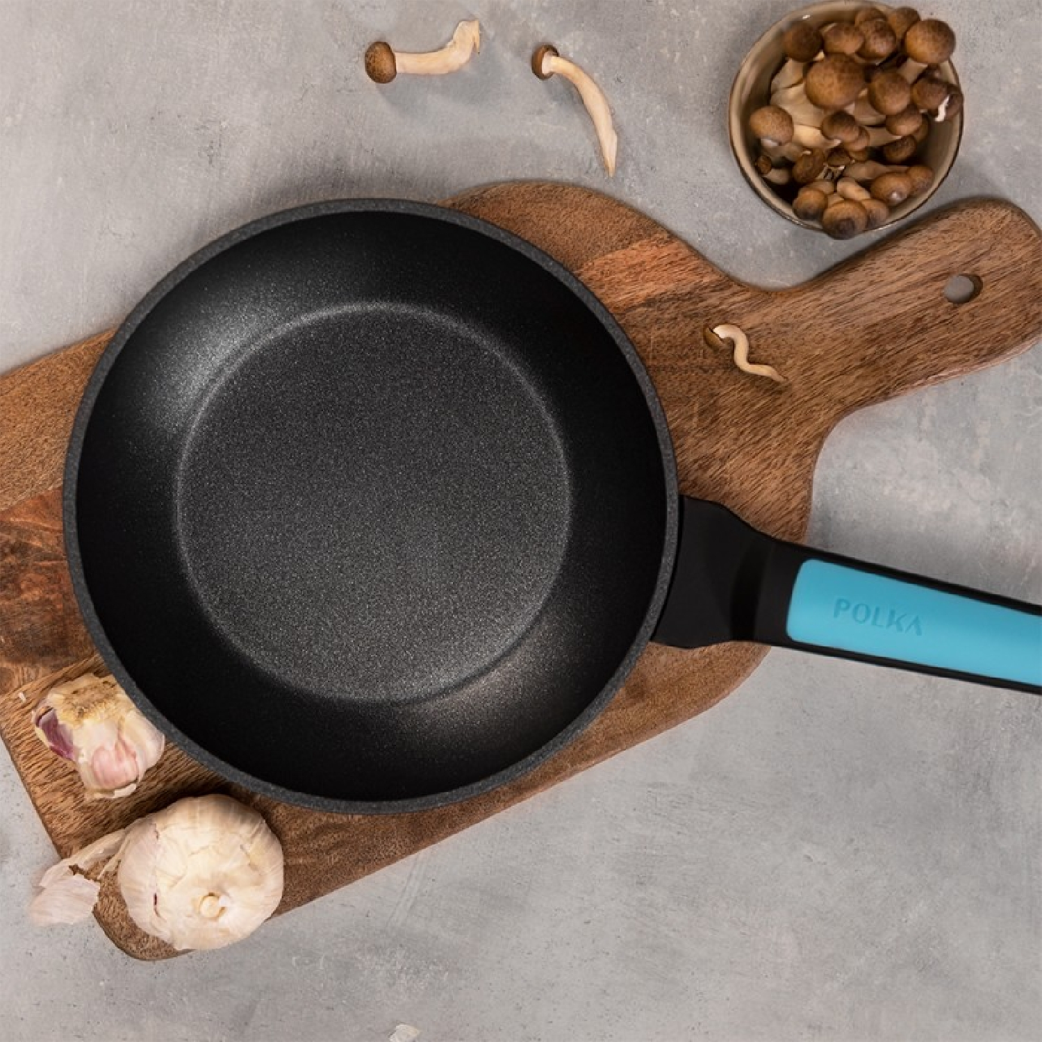 Czarna patelnia z turkusowym uchwytem i składnikami na drewnianej desce.