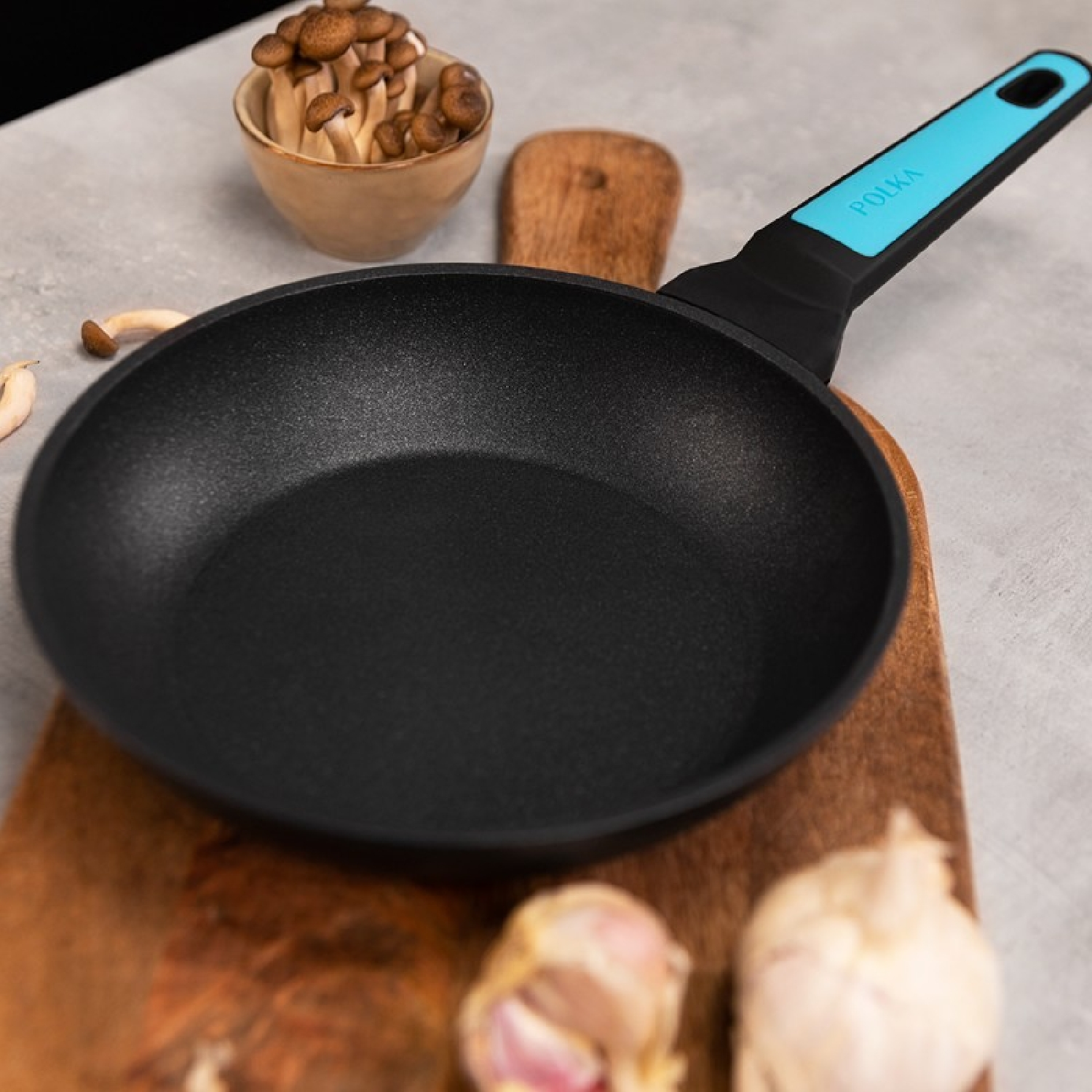 Czarna patelnia z niebieskim uchwytem, ​​na drewnianej desce do krojenia. Grzyby i czosnek.