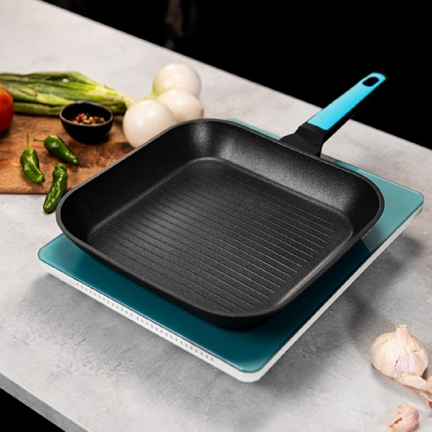 Sartén parrilla negra sobre plato de vidrio azul con verduras y condimentos cerca.