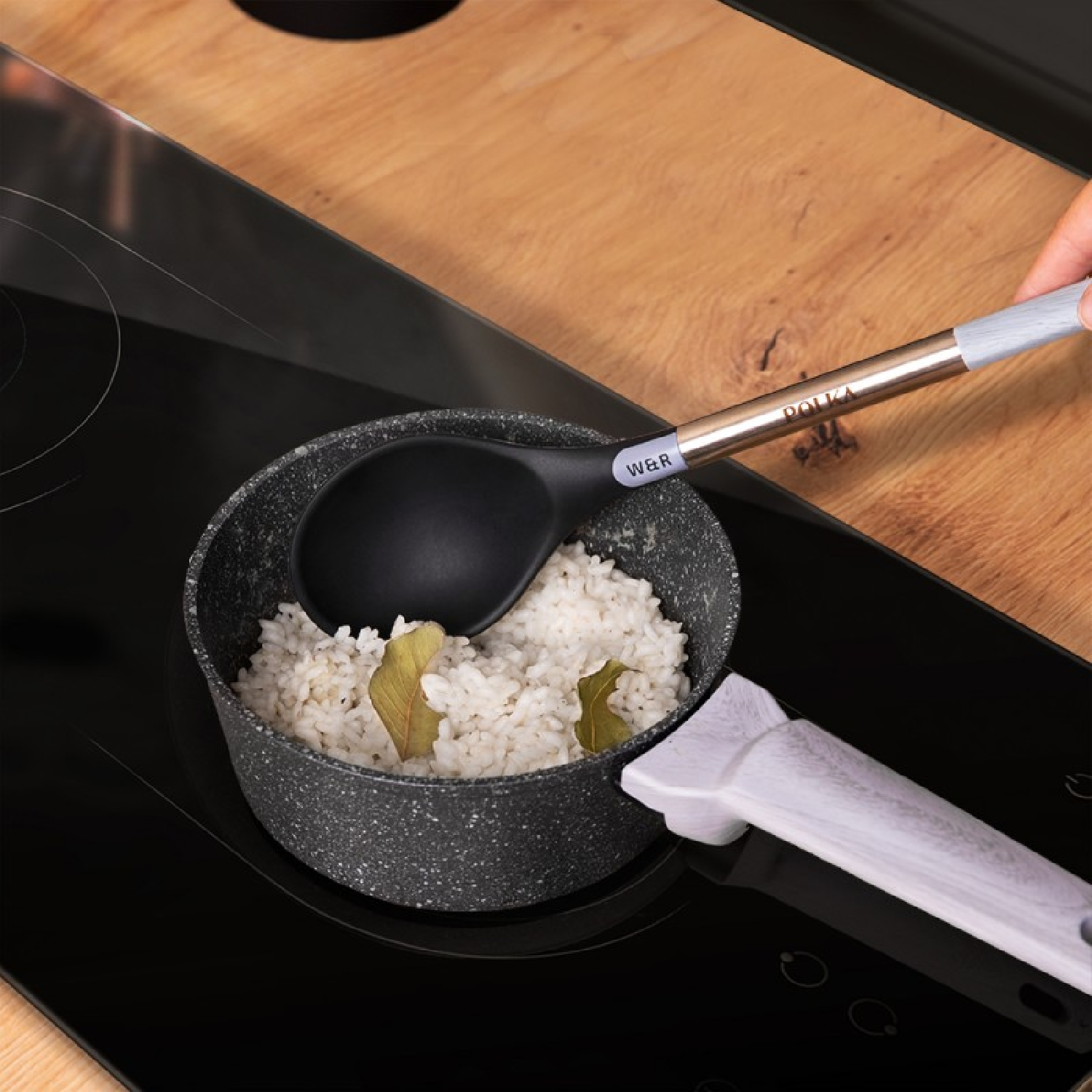 A black spoon scooping rice from a pot on a stove. Wooden countertop.