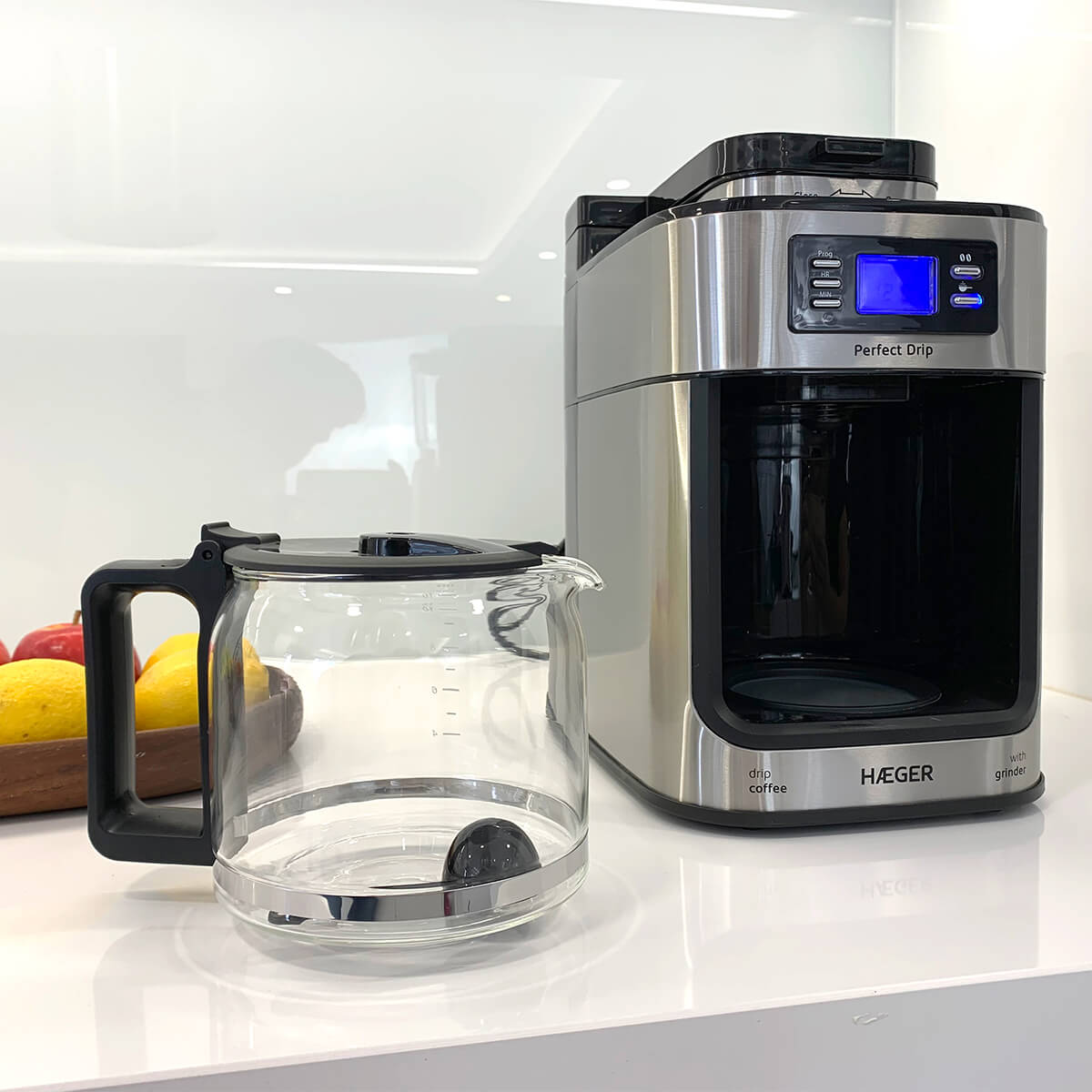 Srebrno-czarny ekspres do kawy ze szklaną karafką na białej powierzchni, w pobliżu cytryny.