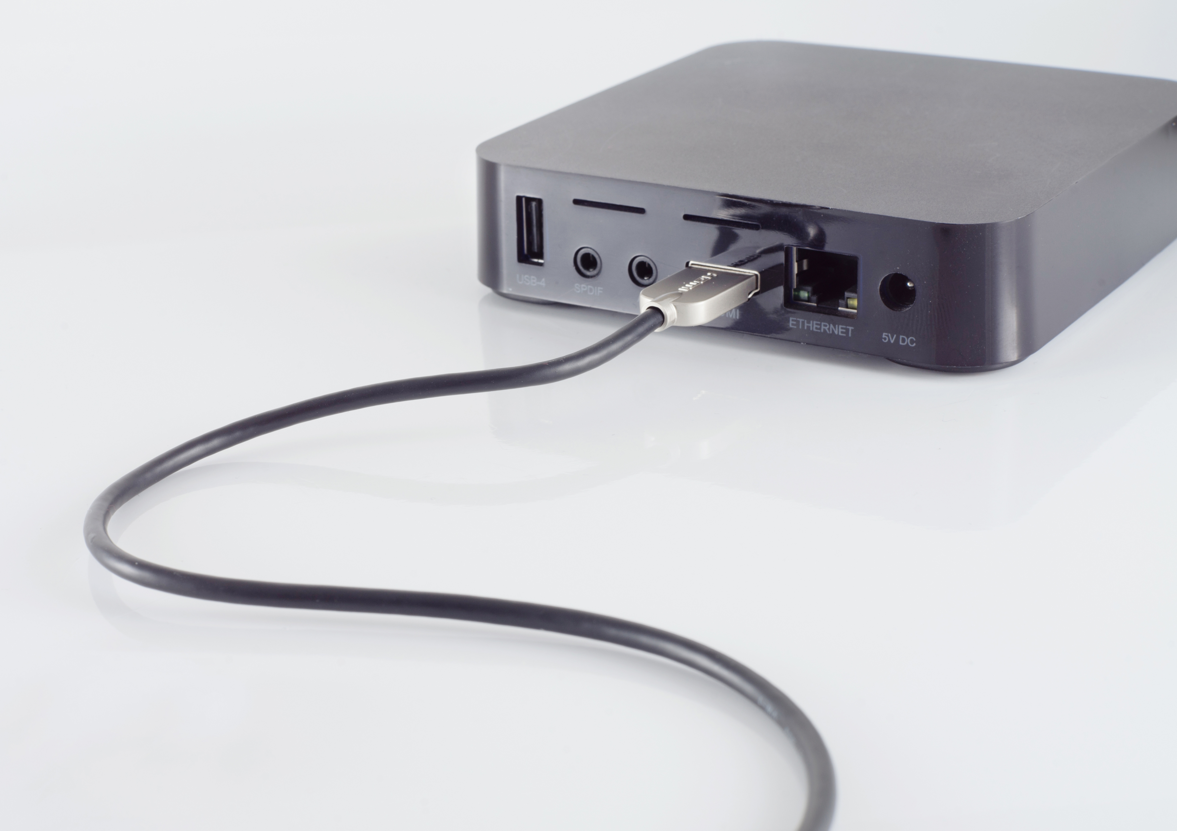 Schwarzes Medien-Streaming-Gerät mit angeschlossenem USB-Kabel auf weißem Untergrund.