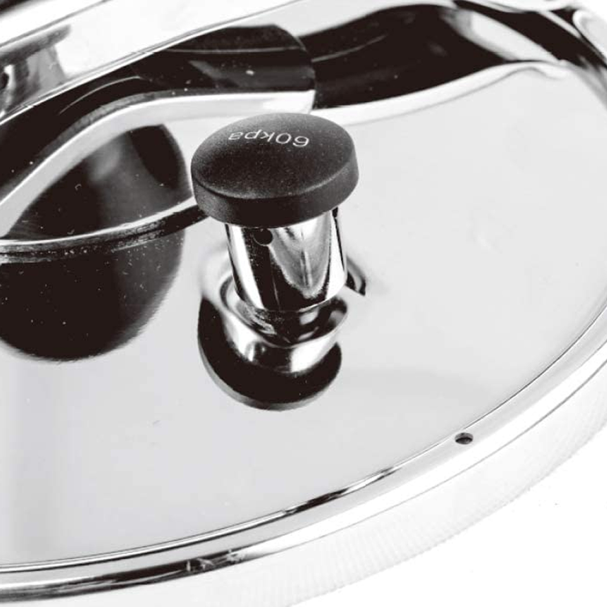 Primer plano de la tapa de una olla a presión. La tapa es plateada brillante. La válvula negra tiene '60 kpa'.