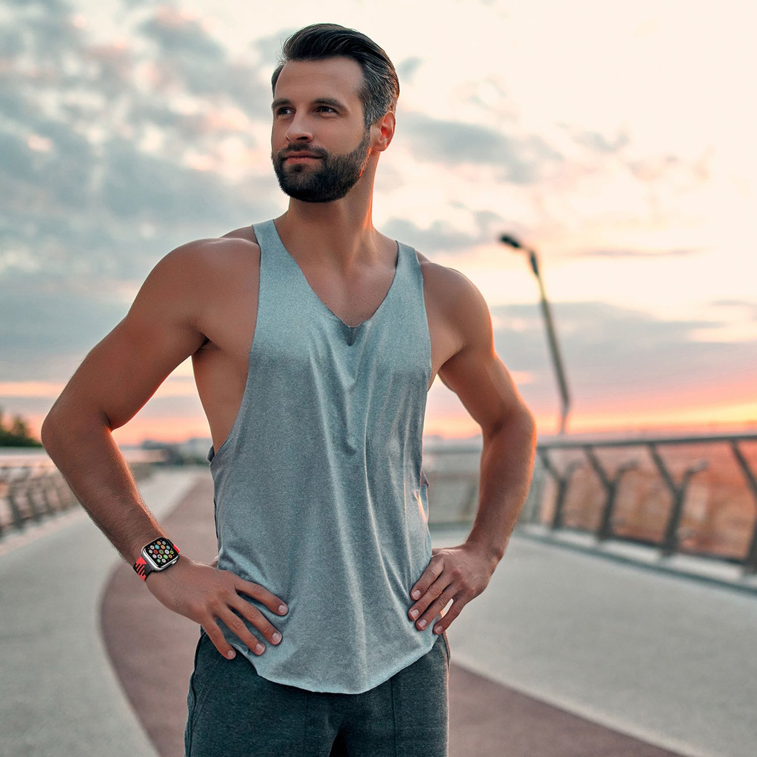 Mann in Tanktop, der wegschaut. Hat eine Smartwatch am Handgelenk und ist draußen.