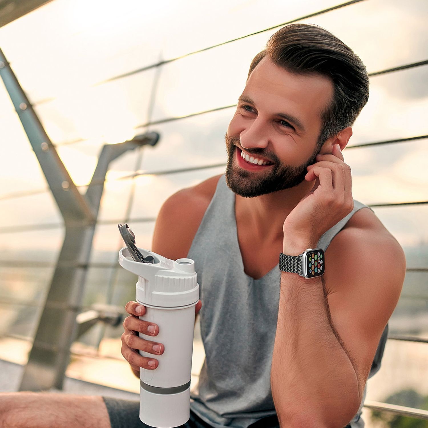 Ein Mann mit Smartwatch, hält eine Wasserflasche und lächelt.