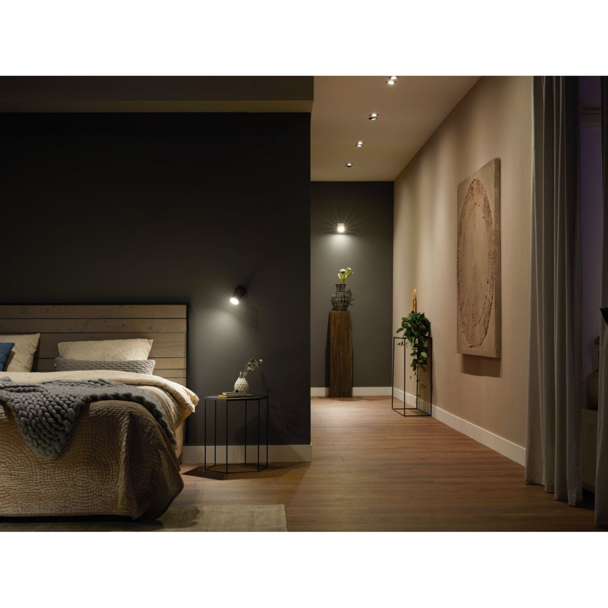 Dormitorio con cama, mesita de noche y luces de pared. Un cuadro cuelga en la pared.