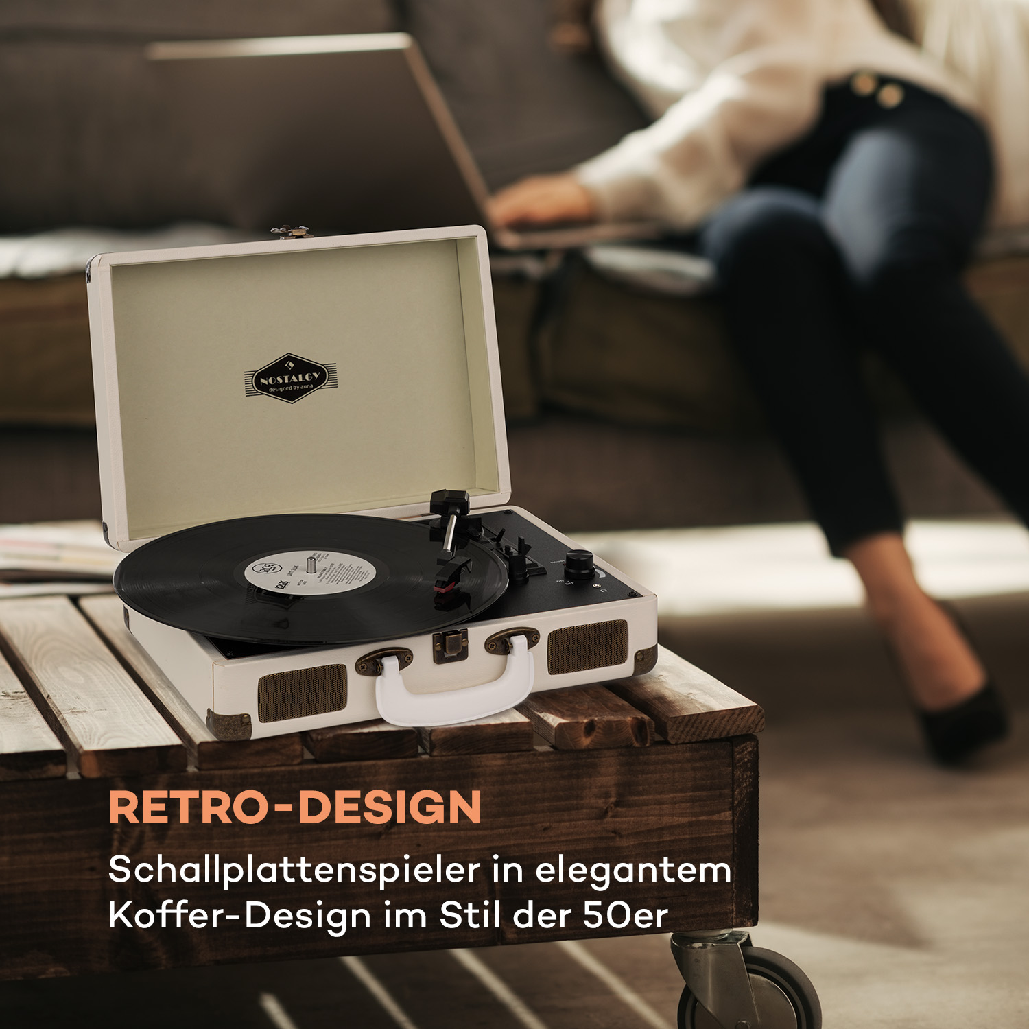 Vintage Plattenspieler auf einem Holztisch. Eine Frau ist im Hintergrund unscharf.