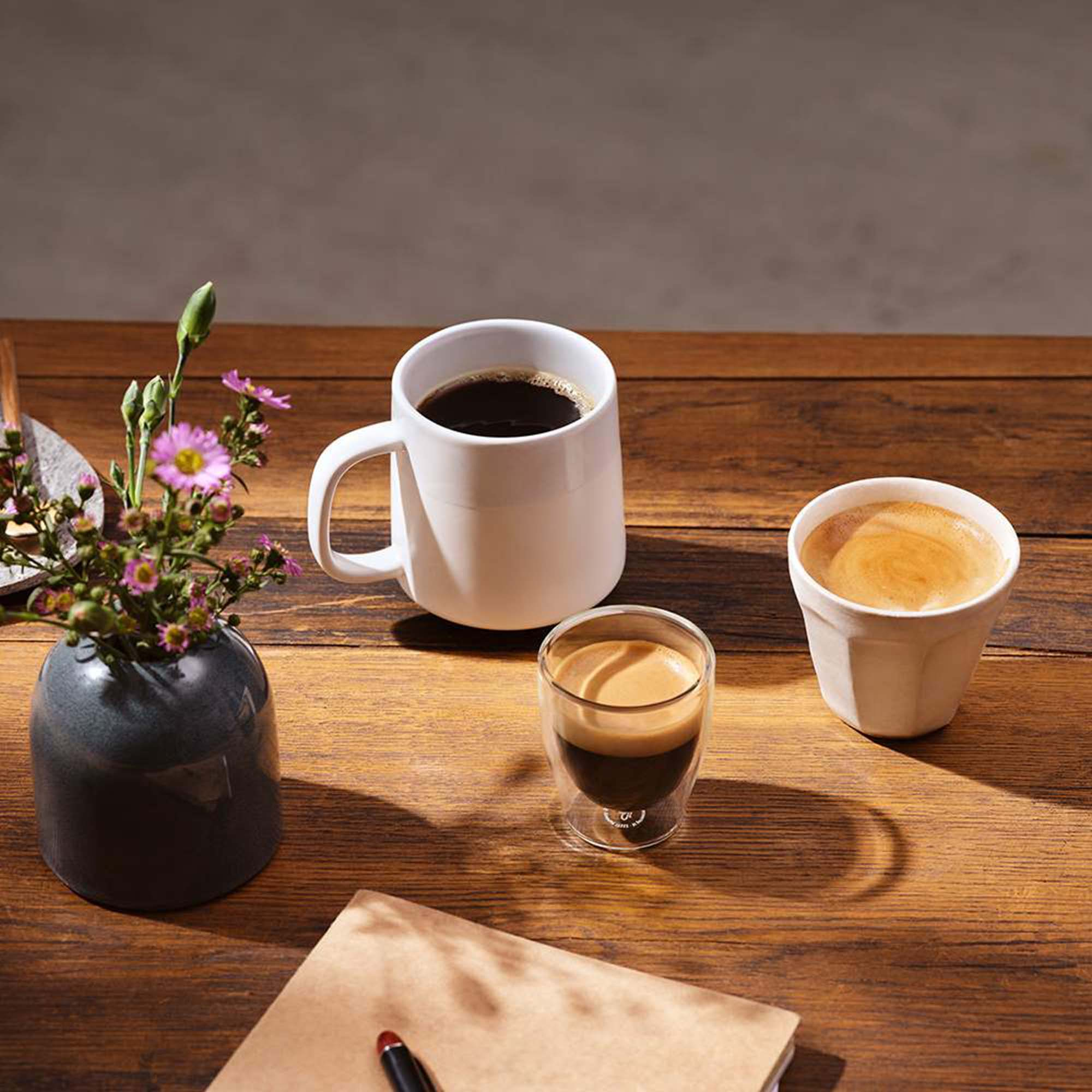 Kaffee und Blumen auf einem Holztisch. Enthält eine Tasse, ein Glas und eine kleine Tasse.