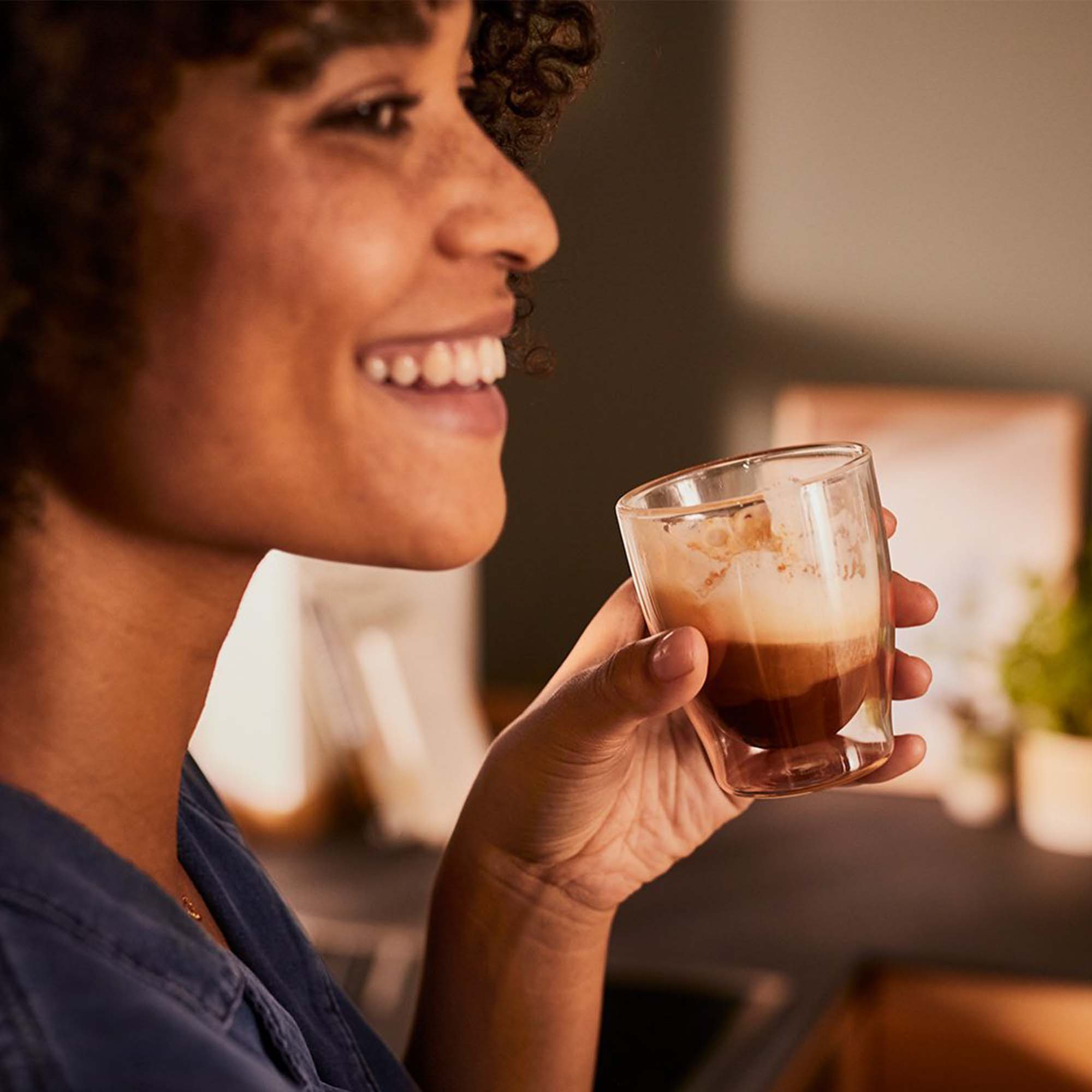 Lächelnde Frau, hält ein Glas geschichteten Kaffees mit Schaum.
