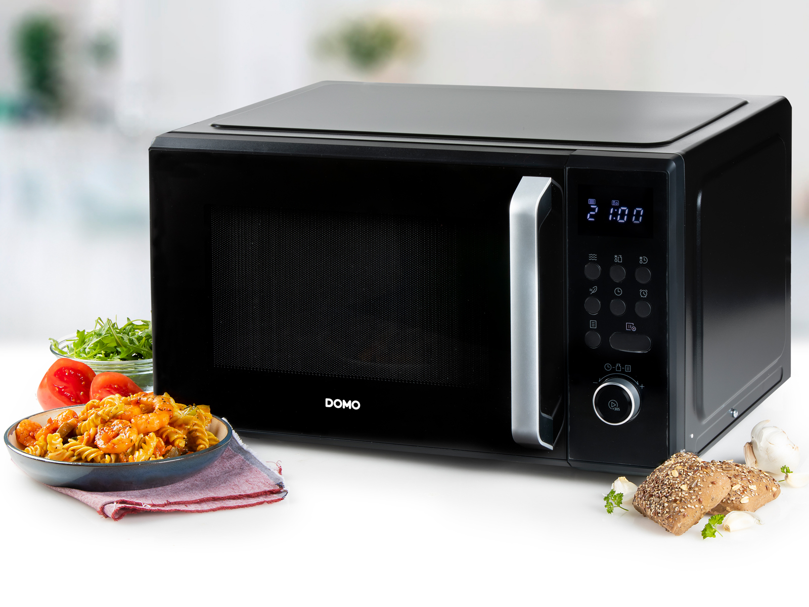 Eine schwarze Mikrowelle mit Digitalanzeige, mit gekochtem Essen und Zutaten im Vordergrund.