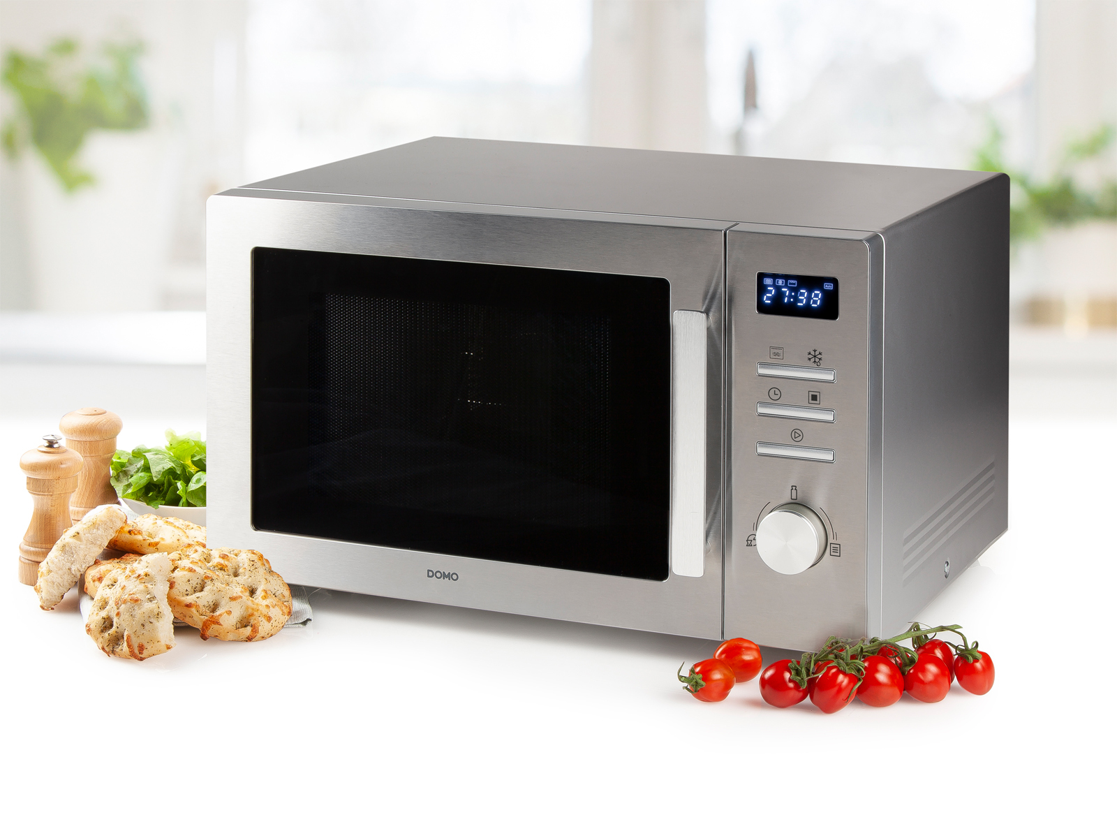 Silberne Mikrowelle mit Digitalanzeige, Lebensmittel links und Tomaten rechts.