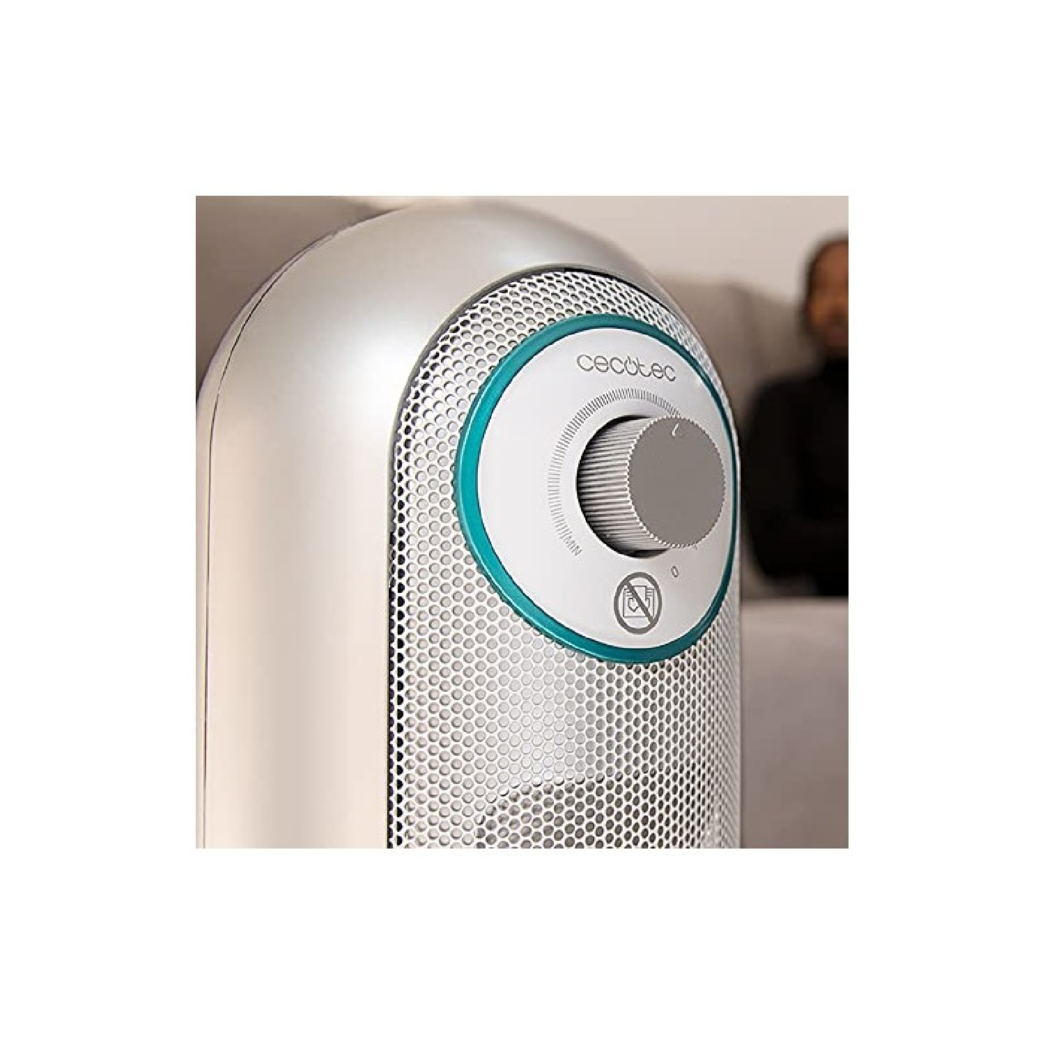 Srebrno-biały grzejnik z pokrętłem i logo Cecotec. Niewyraźna osoba w tle.