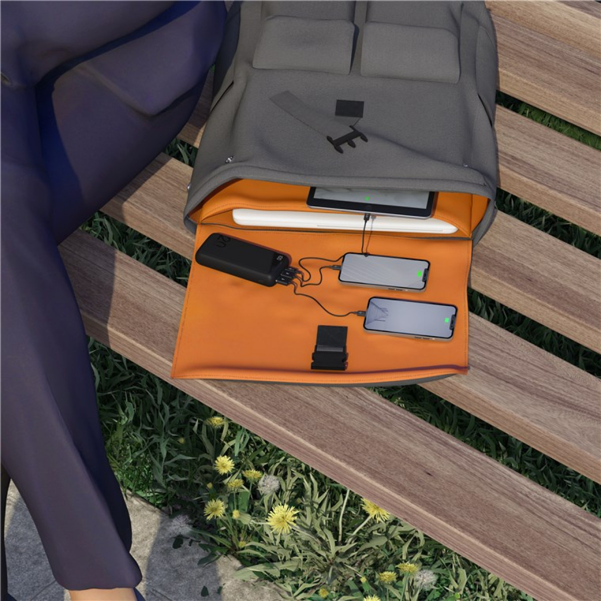 Rugzak open, met een laptop, twee telefoons die opladen en een powerbank, op een parkbank.