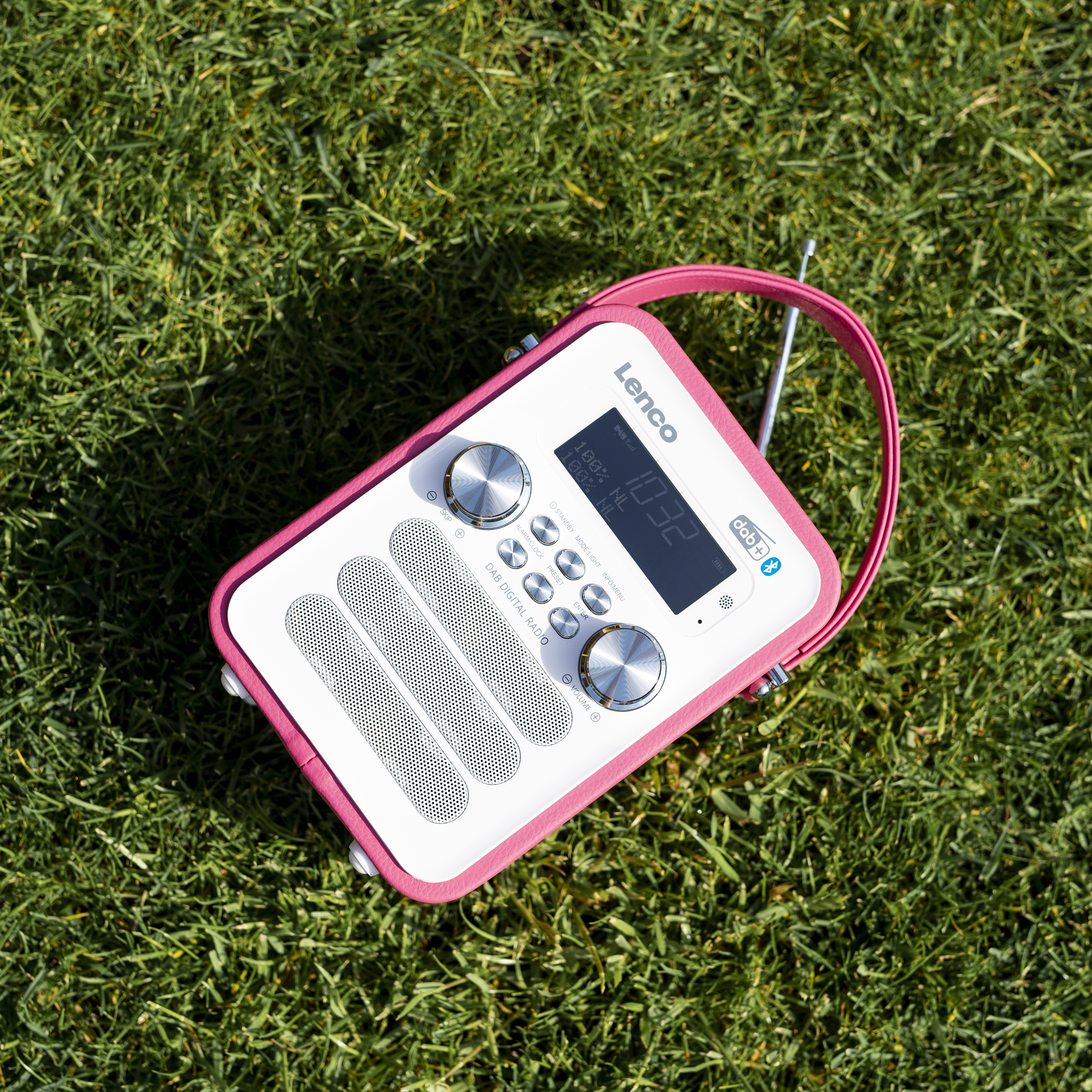 Biało-różowe radio na zielonej trawie, z uchwytem i ekranem.