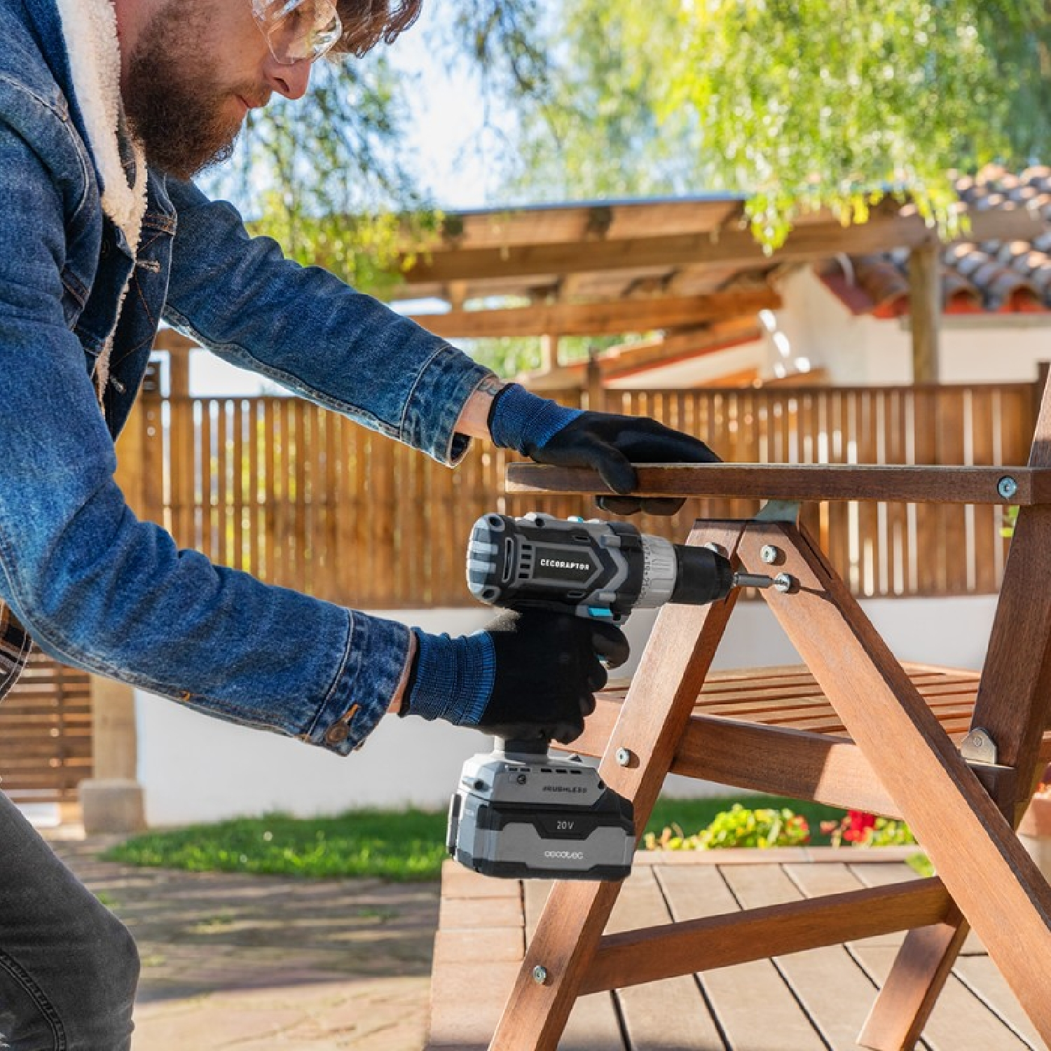 Uomo che usa un trapano avvitatore per assemblare una sedia di legno all'aperto.