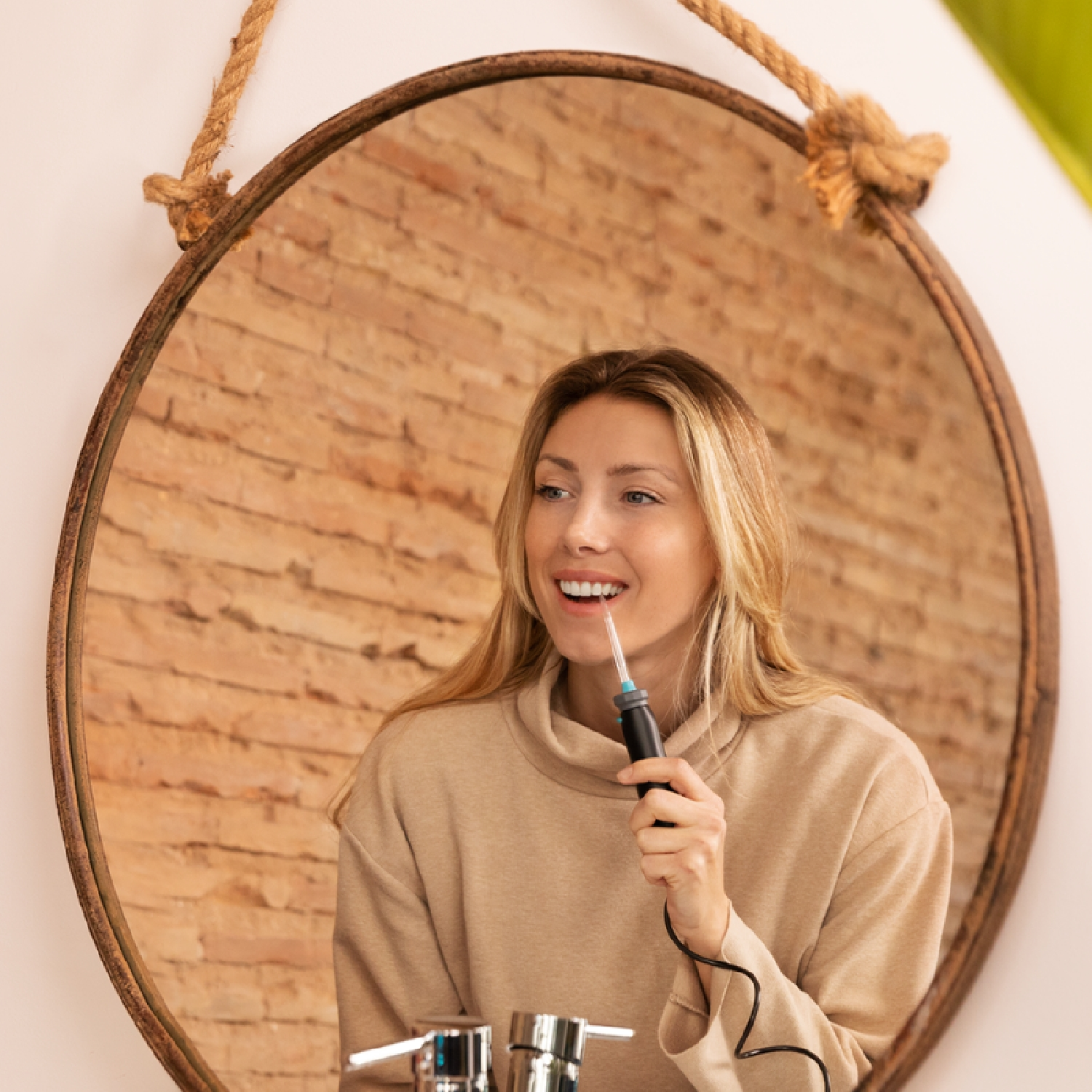 Vrouw lachend, gebruikt een monddouche voor een spiegel. Rustieke bakstenen muur.
