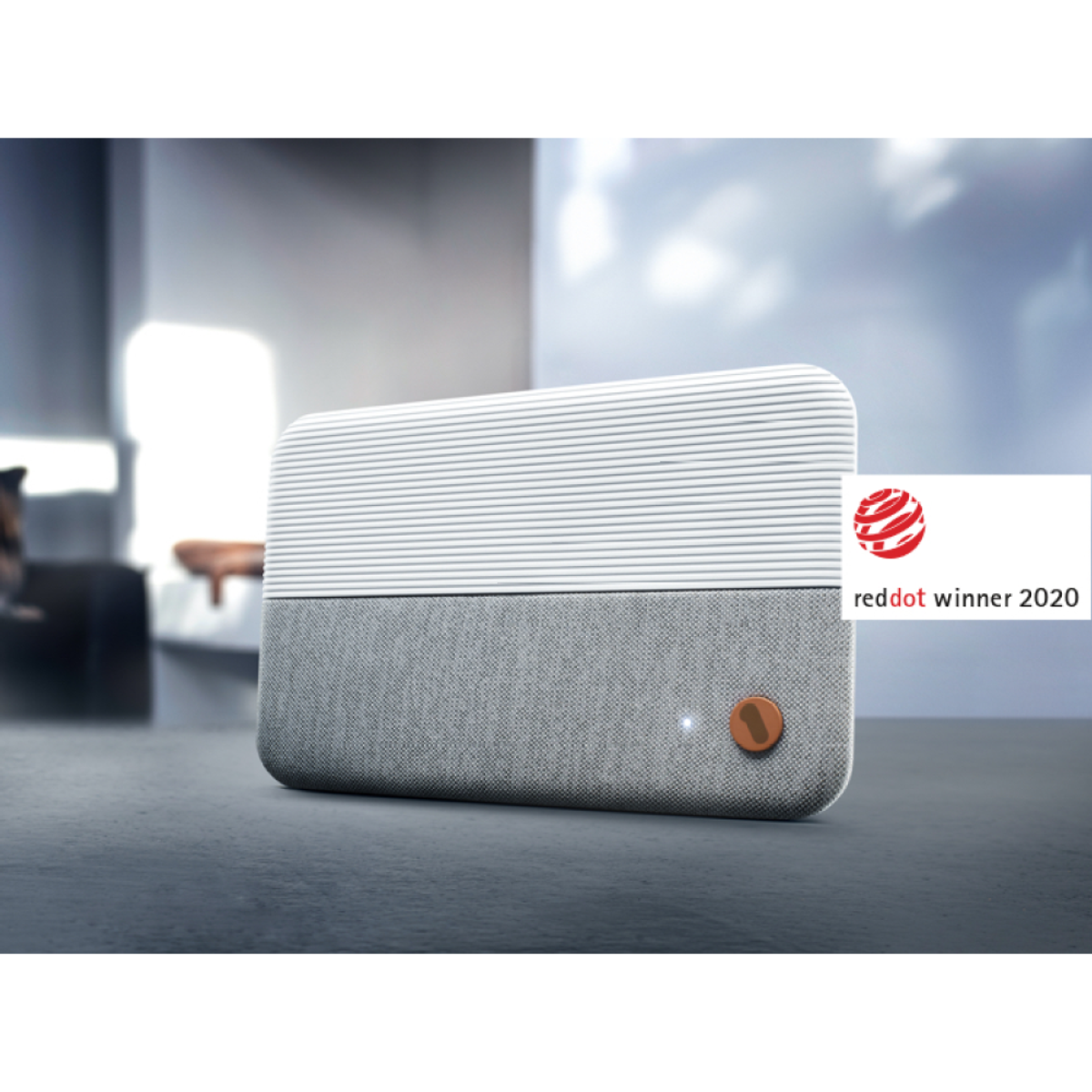 Modern speaker. Gray and white design, with a Red Dot Winner 2020 label. Placed on a surface.