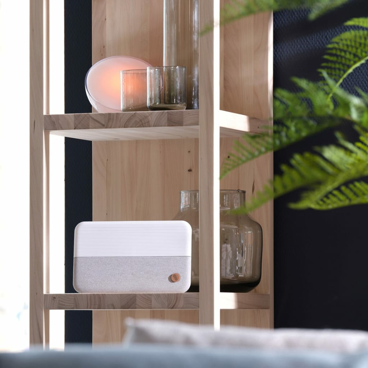 Wooden shelf with a speaker, vases, and a candle. The background is a dark wall.