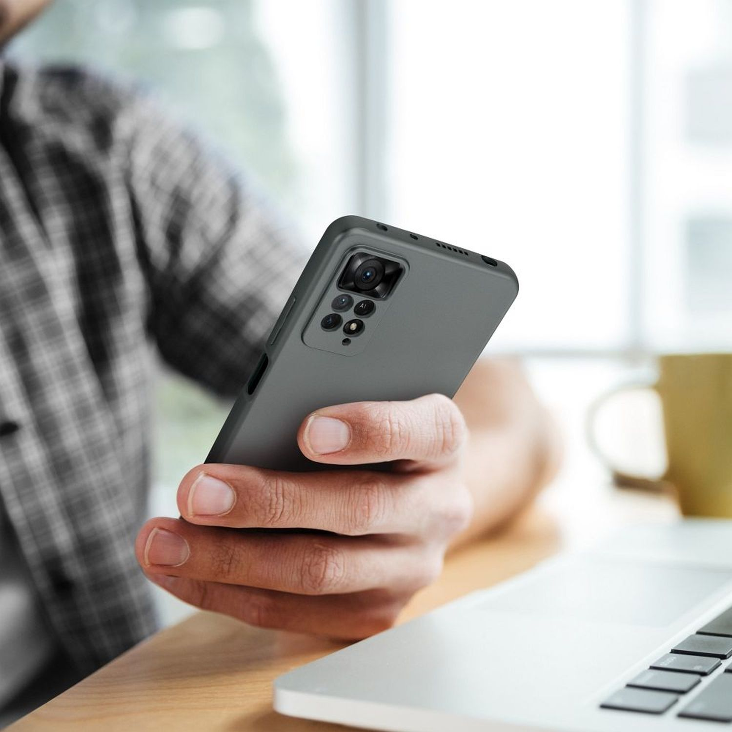 Person hält ein graues Telefon, im Hintergrund ein Laptop.