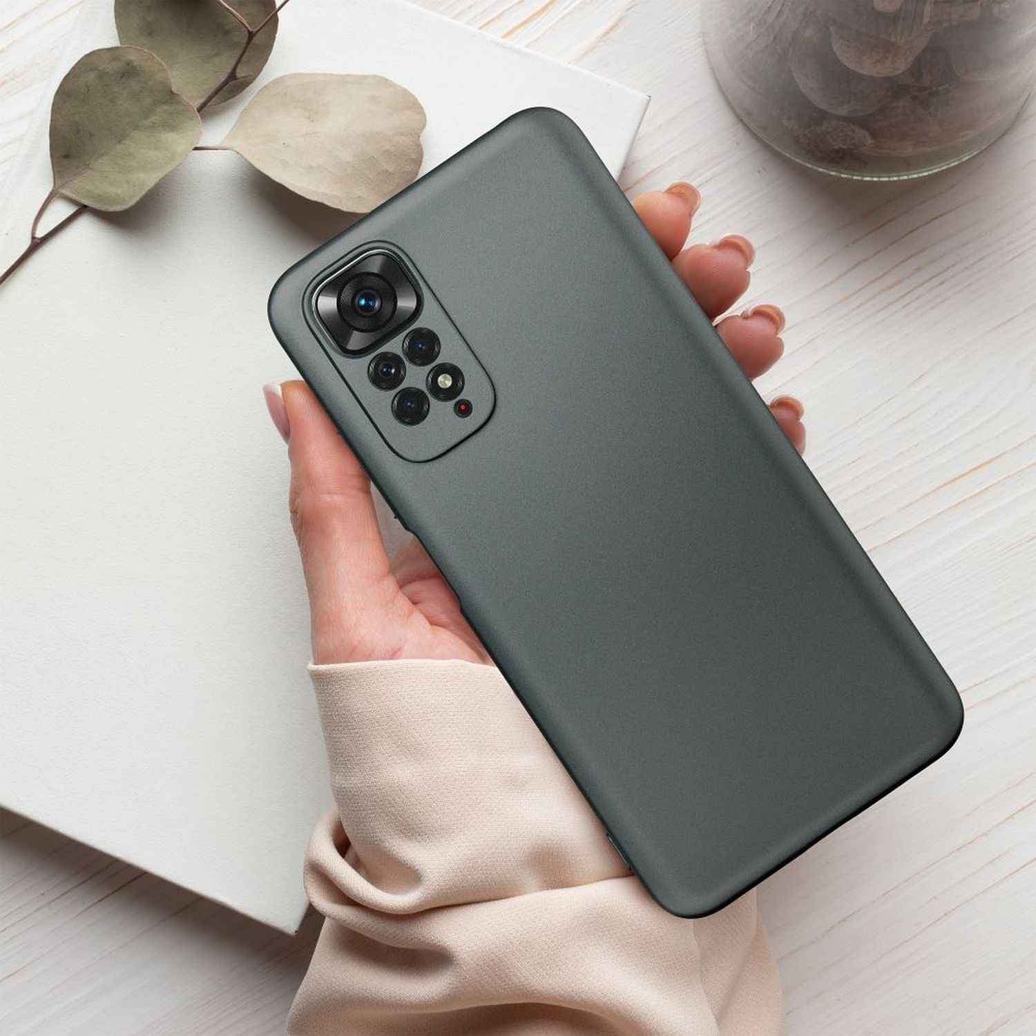 Eine Hand, die eine graue Handyhülle mit einem Telefon darin hält. Der Hintergrund ist ein Holztisch.
