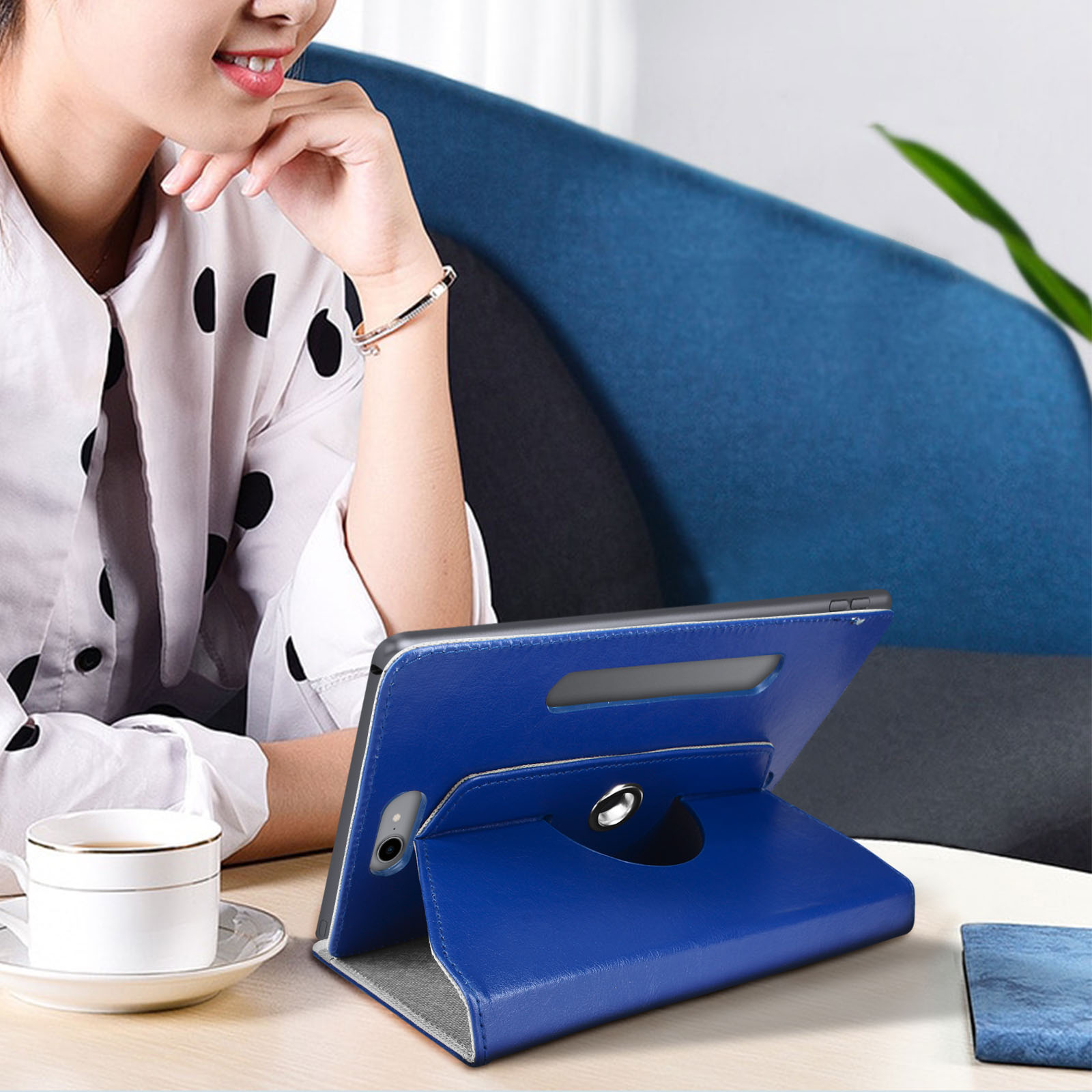 Una donna con un tablet in una custodia blu è seduta vicino a una tazza bianca e a un tavolo.