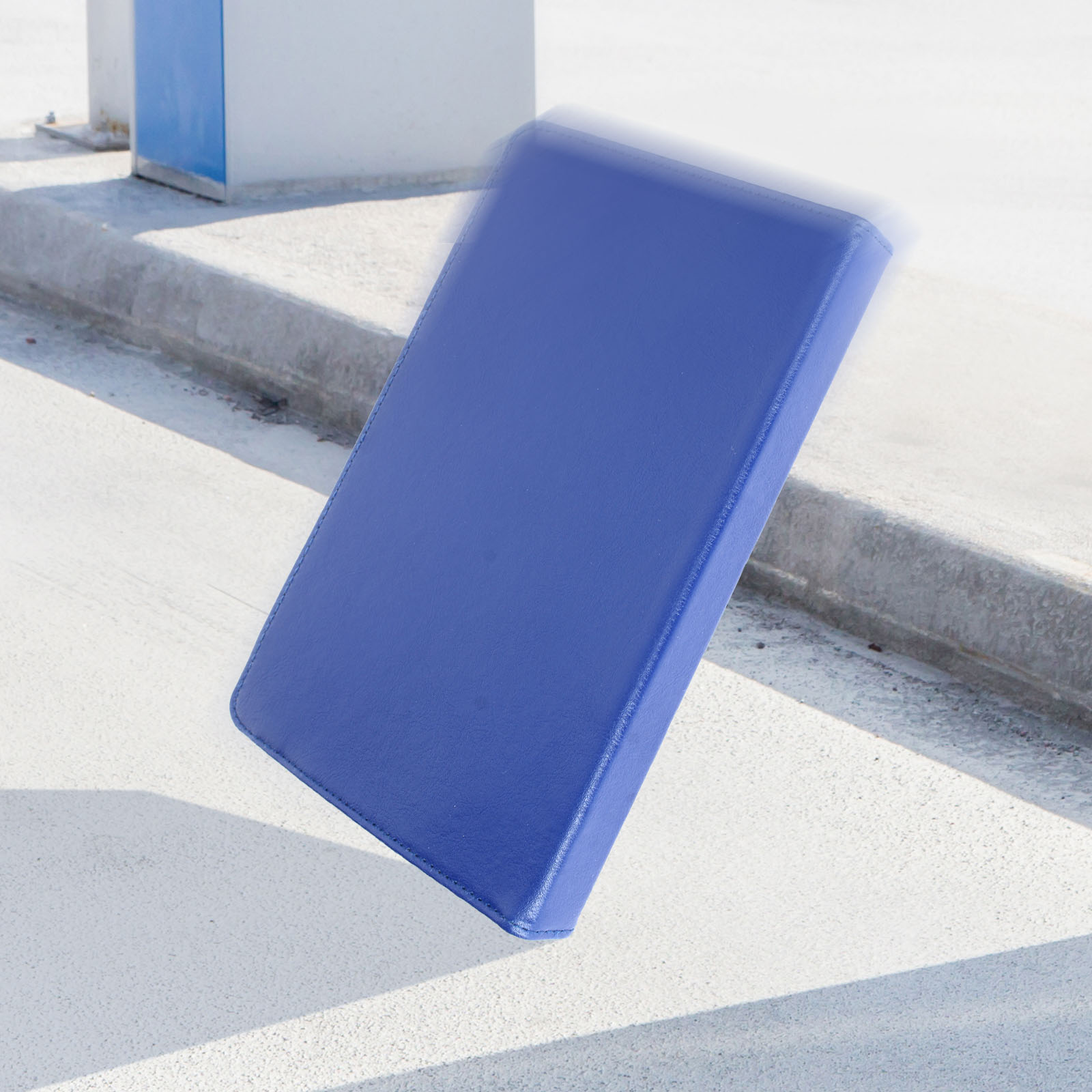 Tablet blu che cade, pavimento in cemento, sfondo sfocato.