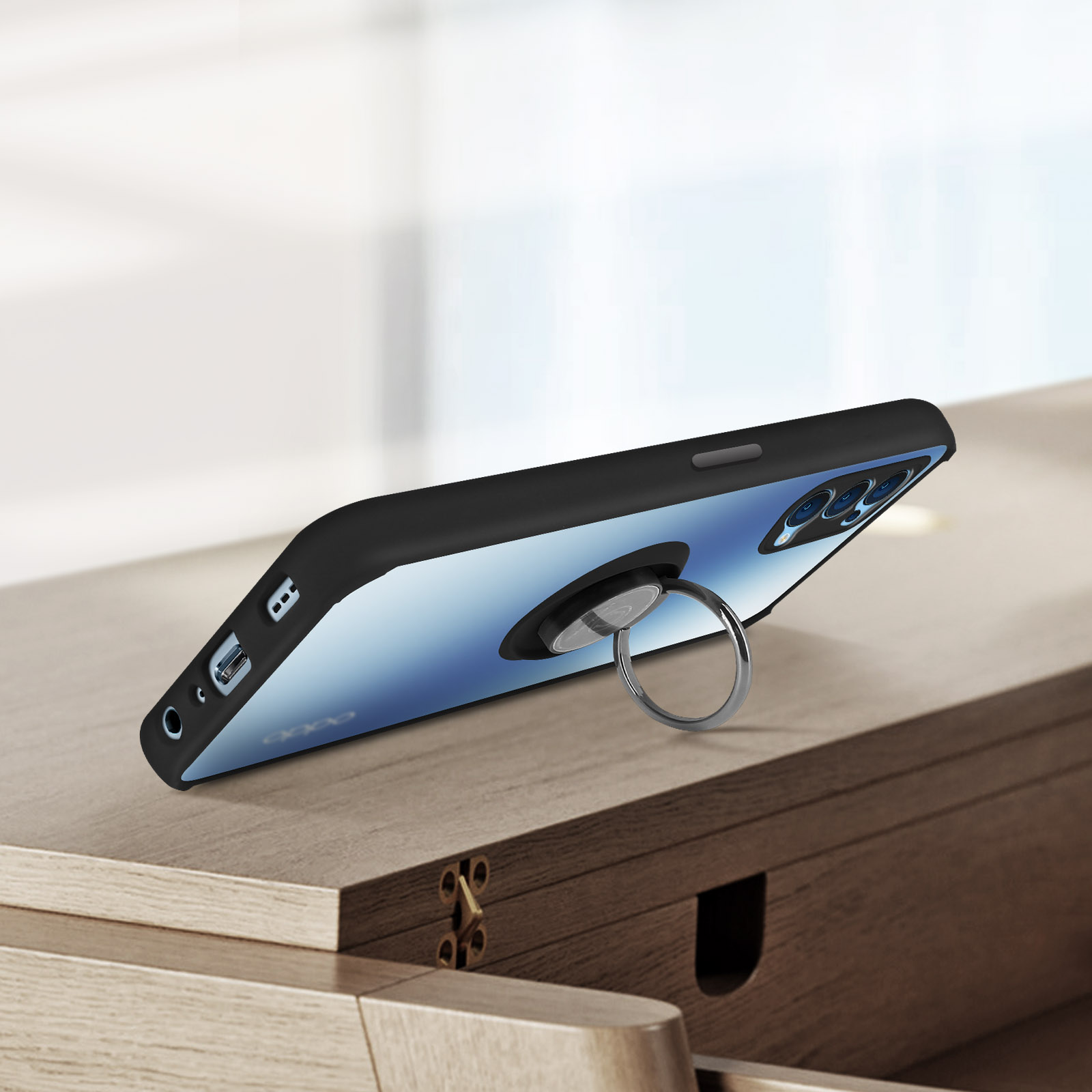 Custodia nera per telefono con anello argentato. Il telefono è appoggiato su una superficie di legno.