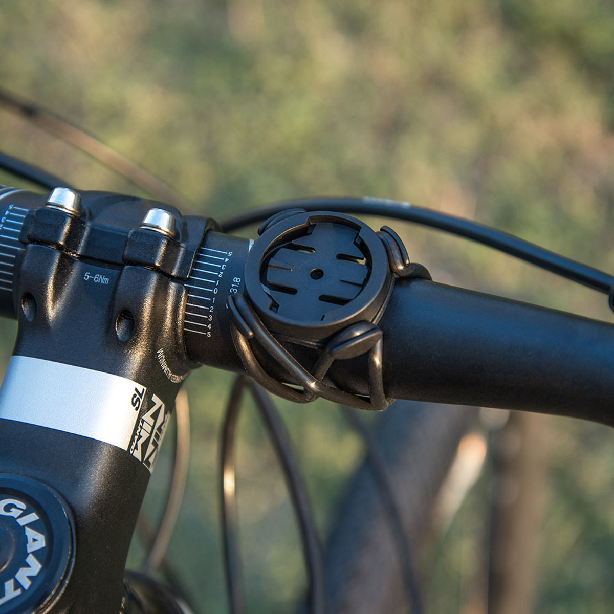 Schwarze Fahrradcomputerhalterung an einem schwarzen Lenker befestigt. Grünes Gras im Hintergrund.