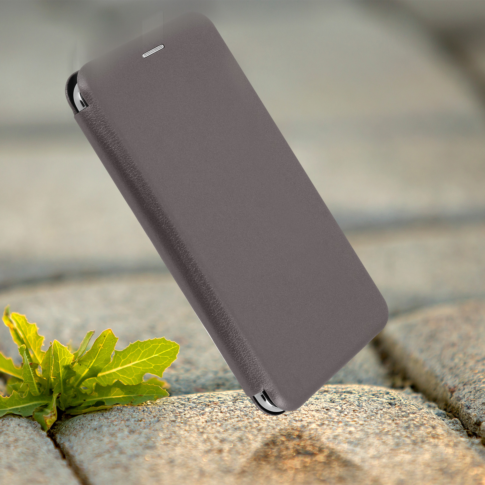 Una custodia marrone per telefono cade su un sentiero di pietra con una pianta verde in primo piano.