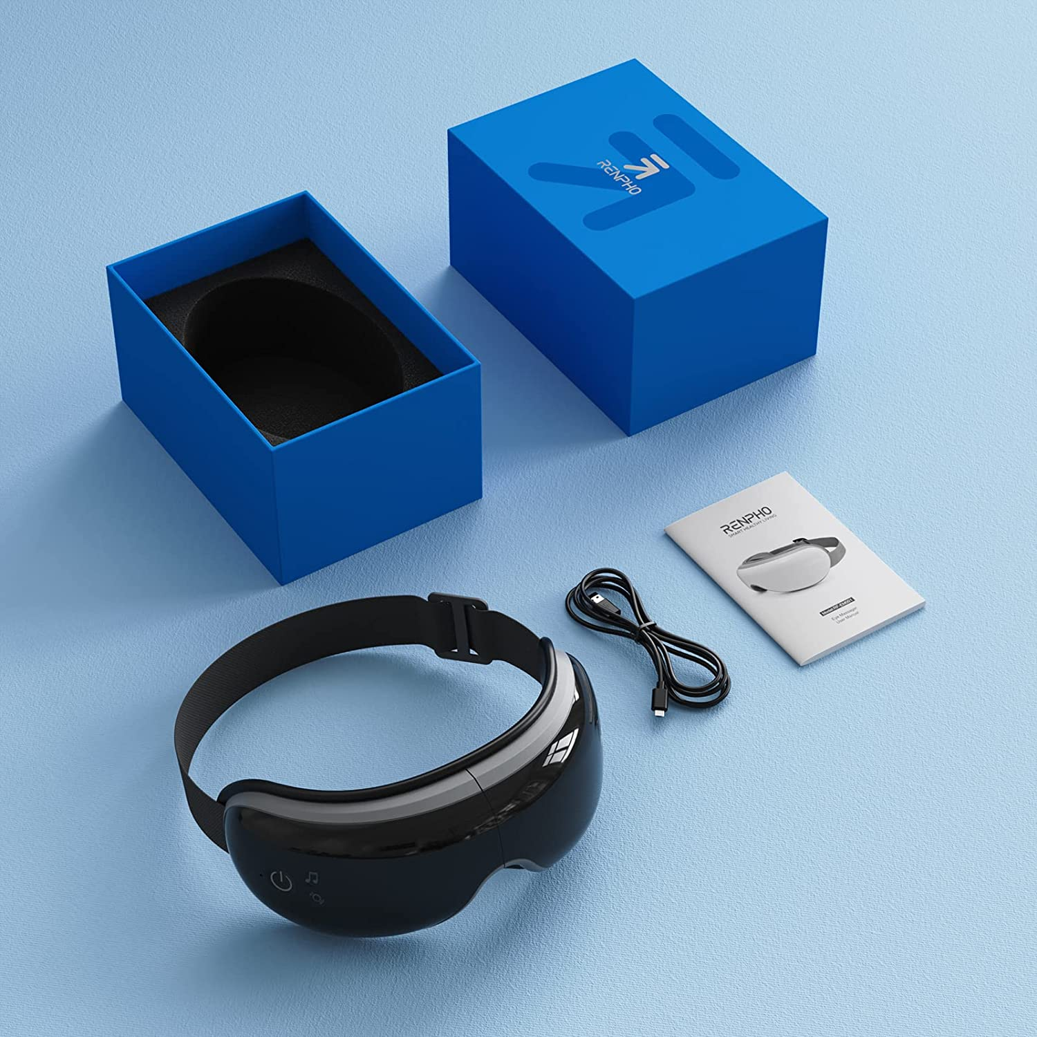 Augenmassagegerät, Box und Zubehör auf blauer Oberfläche. Box hat Logo. Weißes Heft.