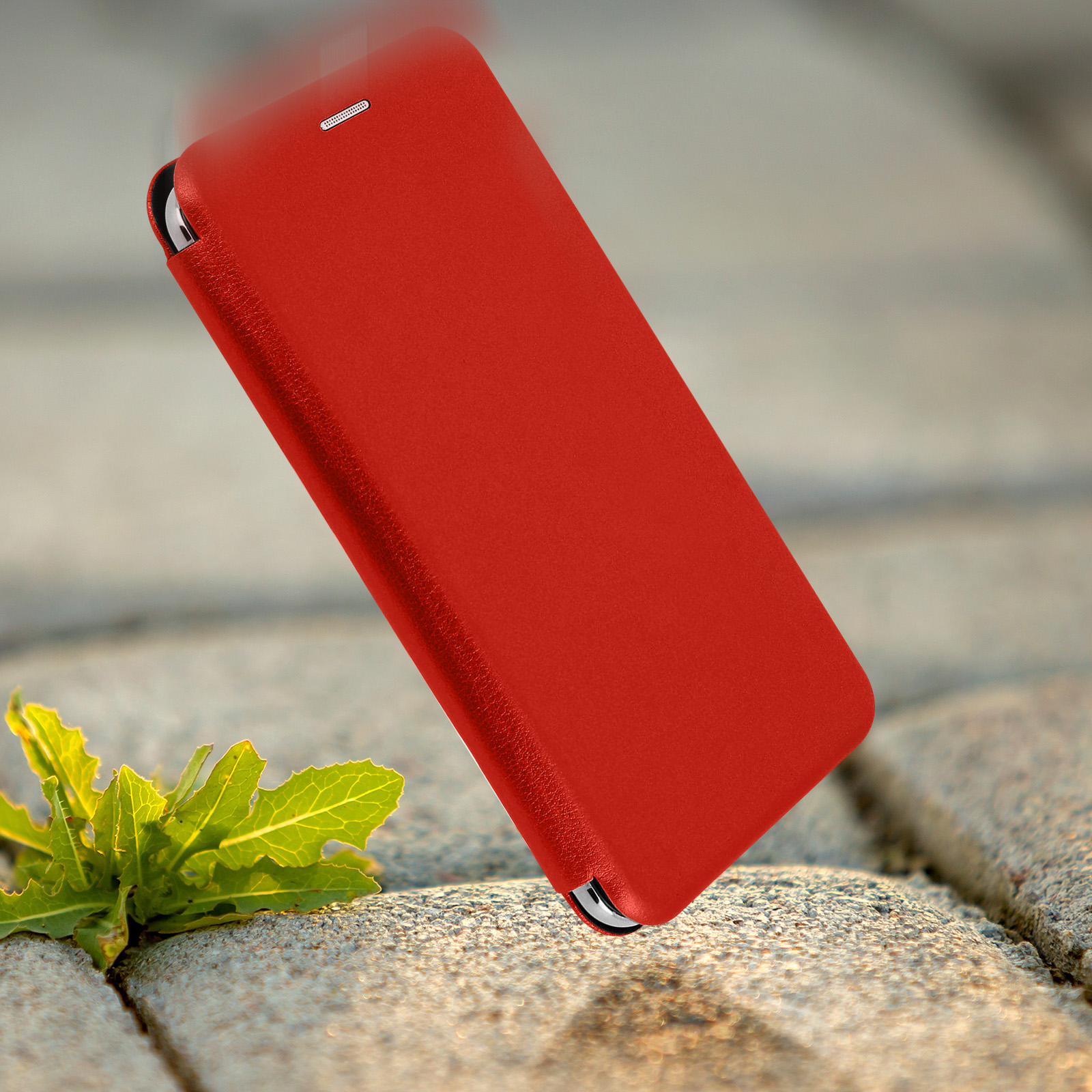 Custodia rossa per telefono che cade a terra. Pianta verde davanti, sfondo sfocato.
