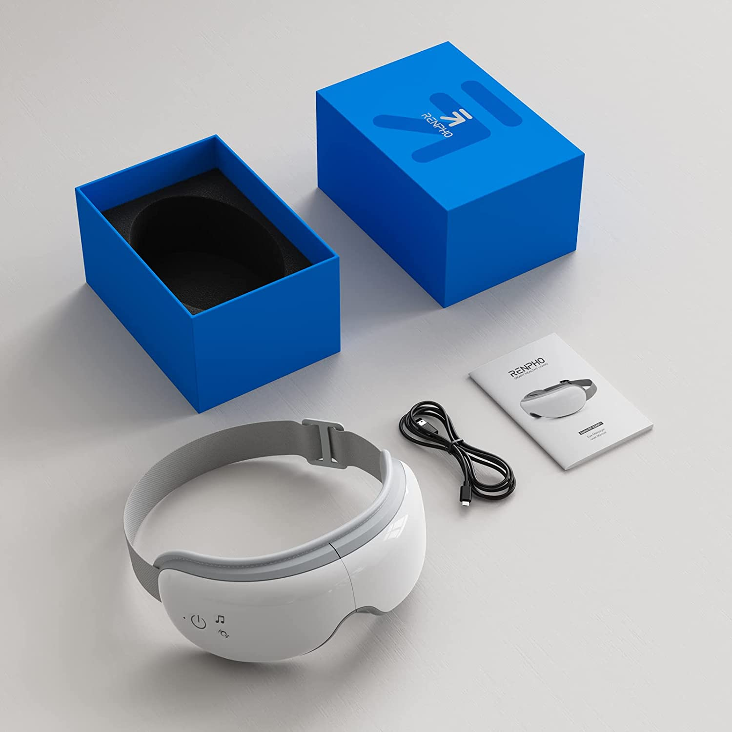 Augenmassagegerät, Box, USB-Kabel und Handbuch auf weißer Oberfläche.
