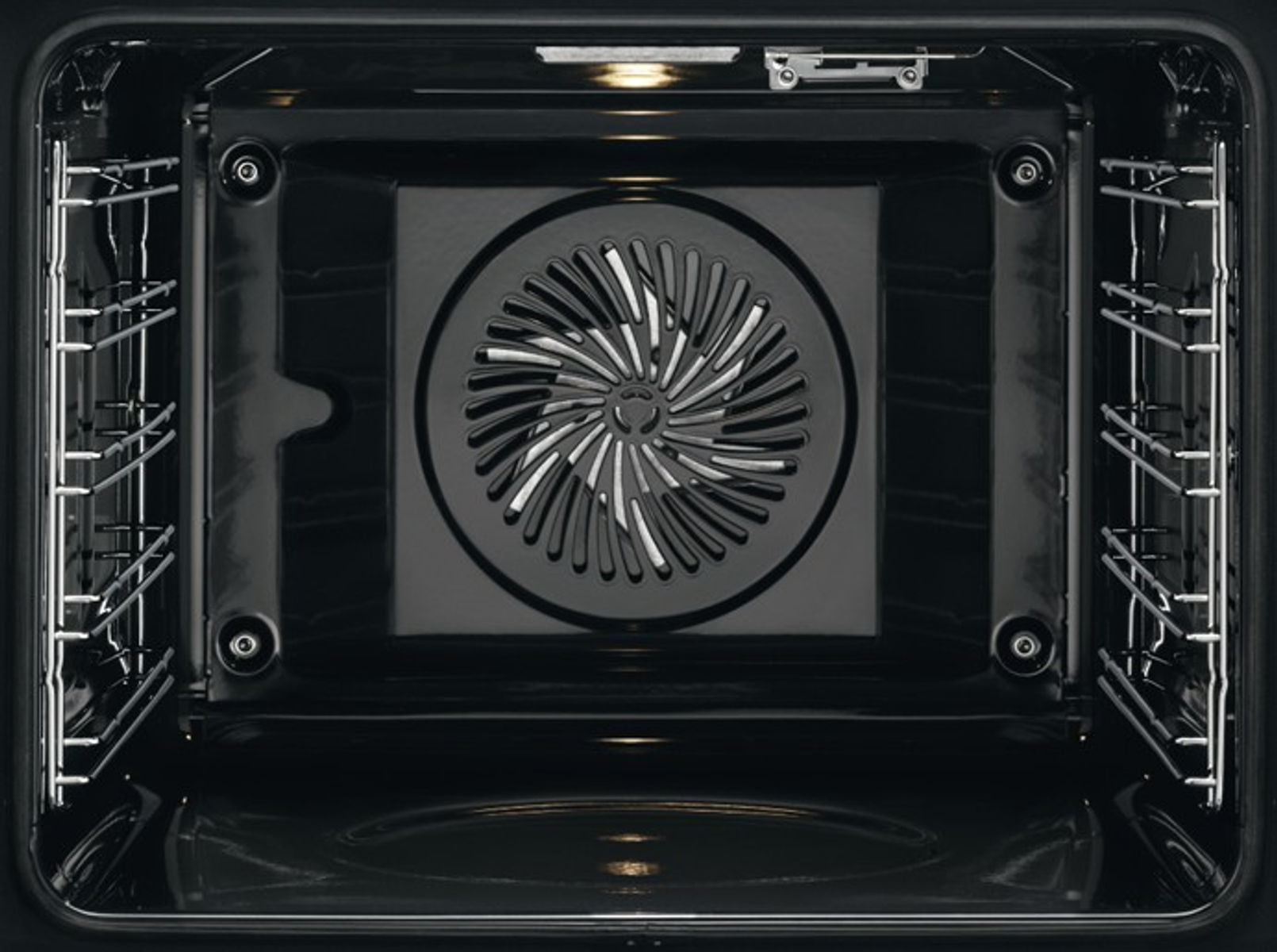Vista interior de un horno negro. Un ventilador en el centro. Estantes de metal a ambos lados.