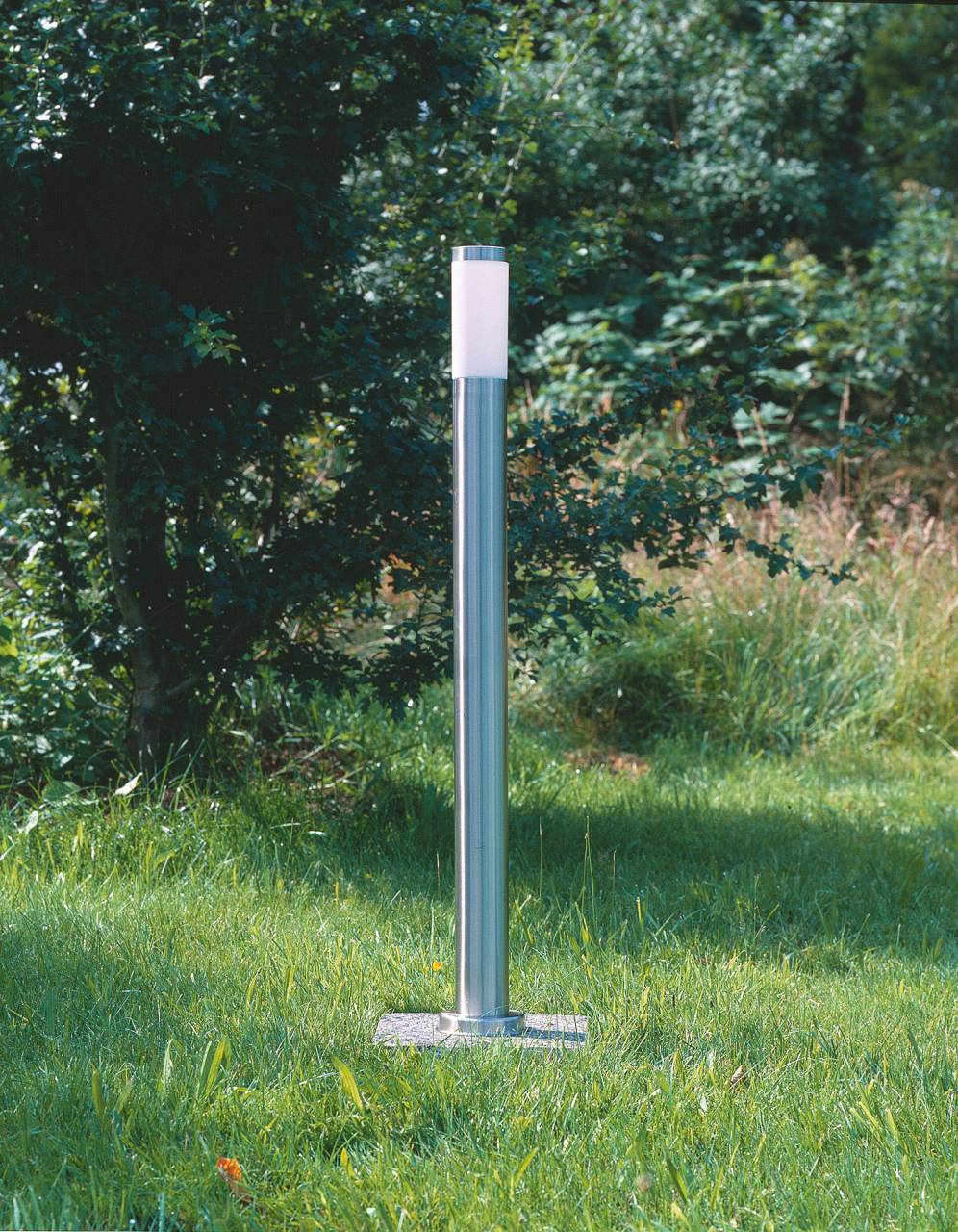 Ein moderner Edelstahl-Gartenpfosten mit weißem Lichtaufsatz steht im Gras.