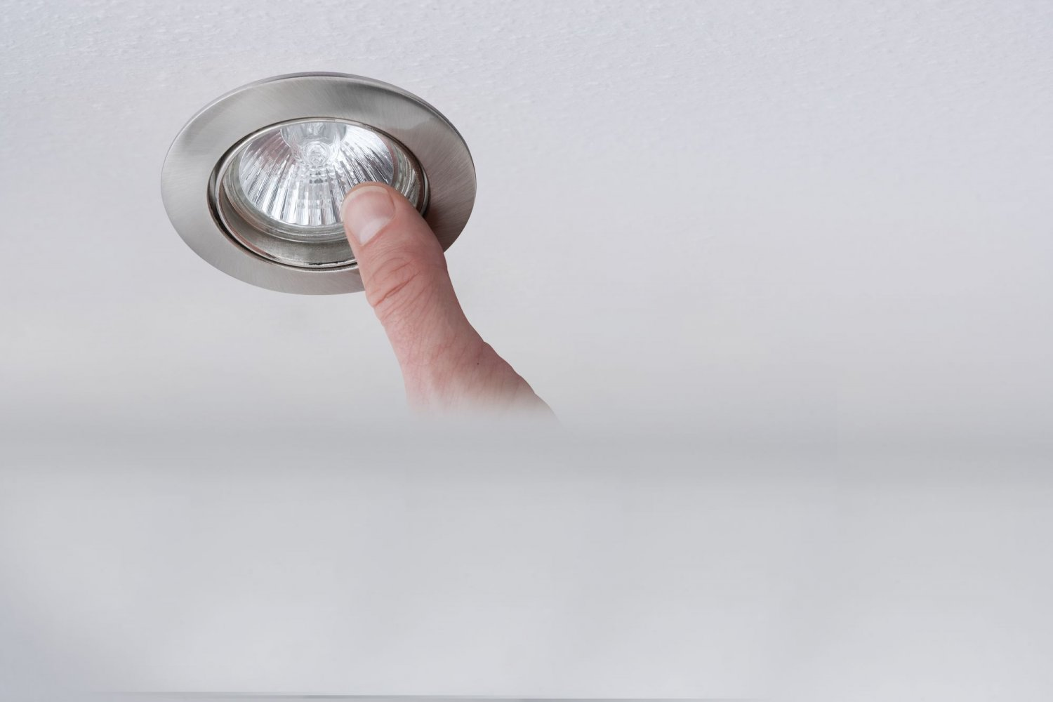 Finger berührt eine Einbauleuchte, die in einer weißen Decke installiert ist, drinnen.