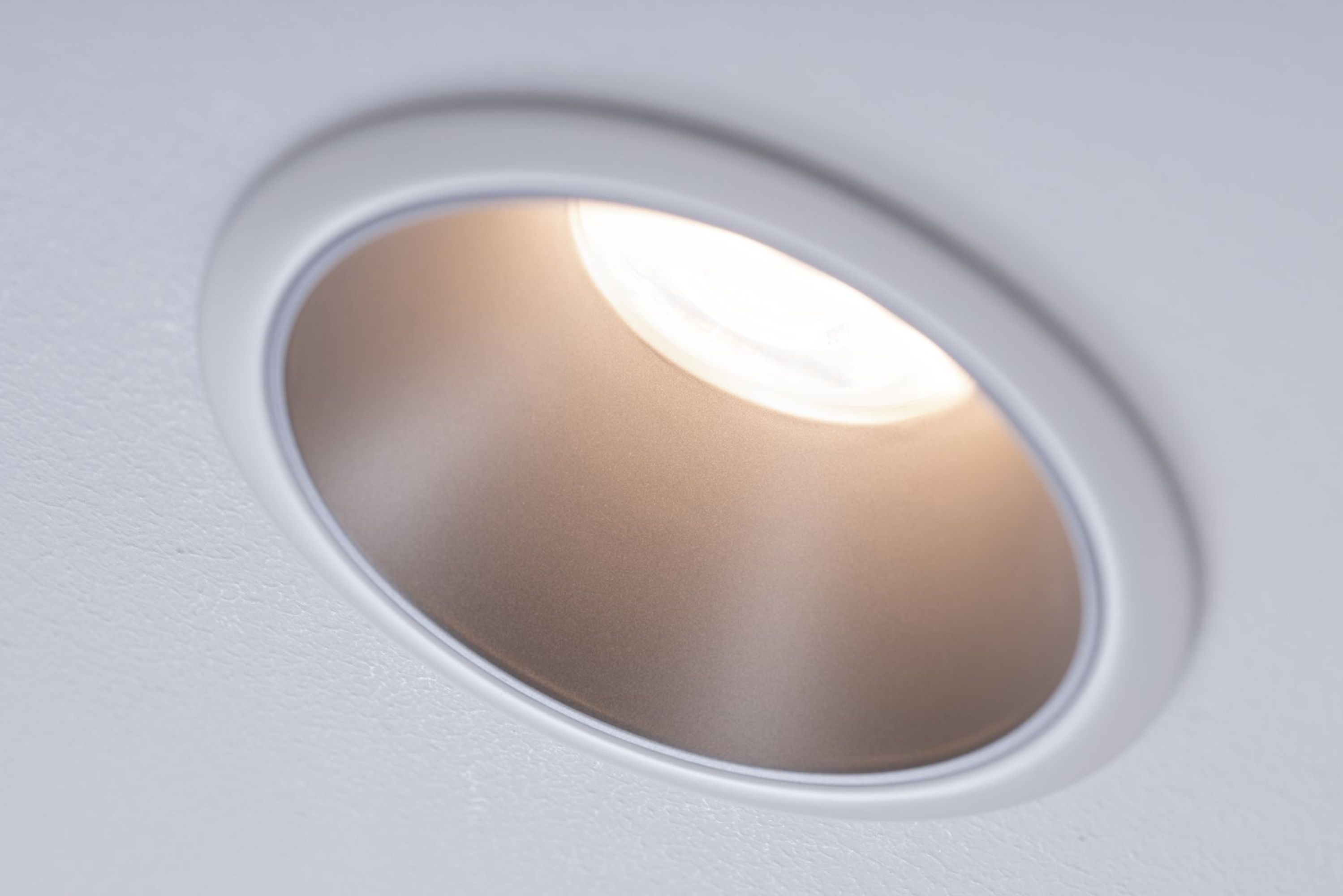 Primo piano di un apparecchio di illuminazione ad incasso, che illumina un interno bianco.