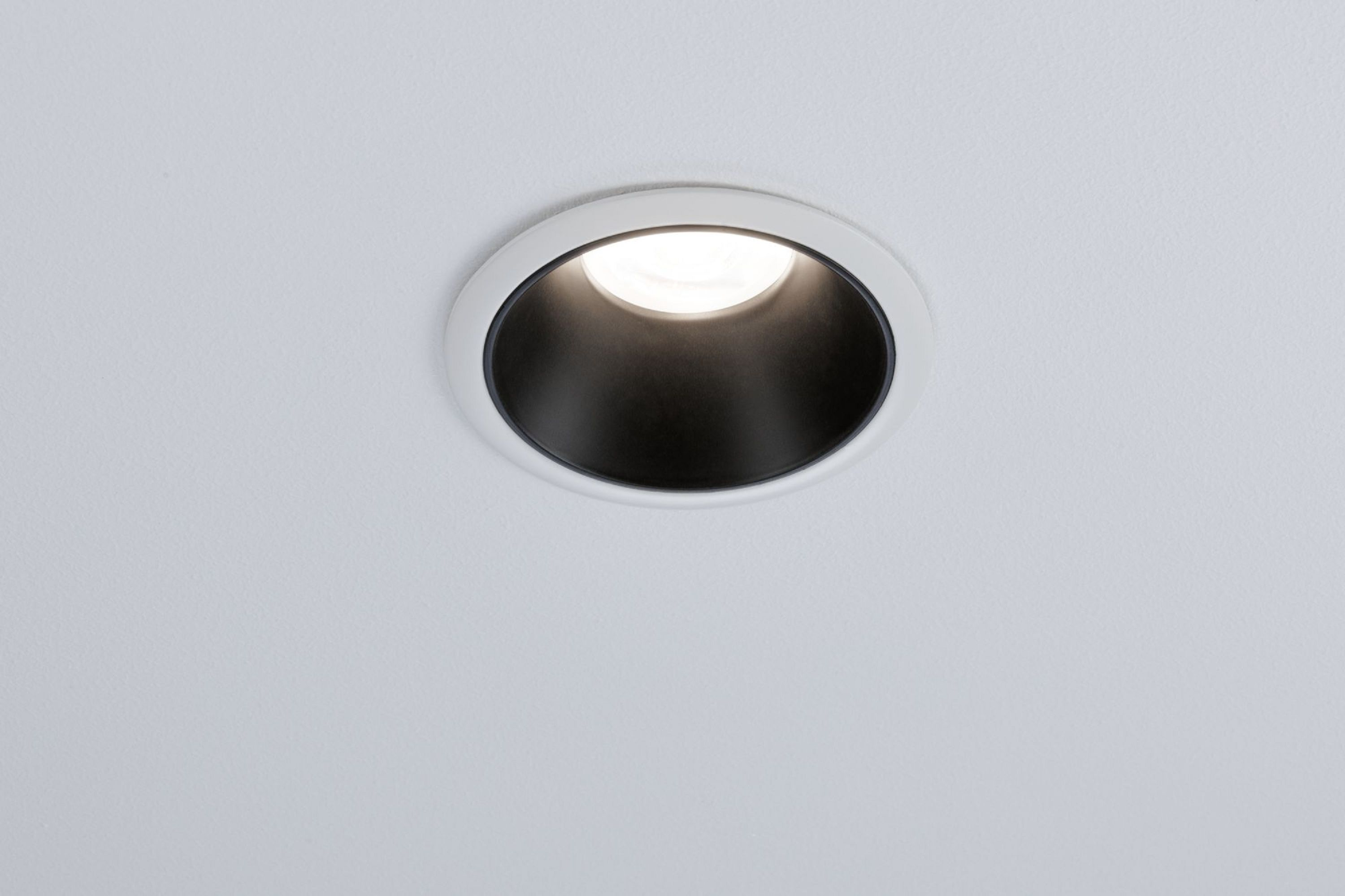 Un faretto da soffitto a incasso con interno nero e finiture bianche, che emette luce.