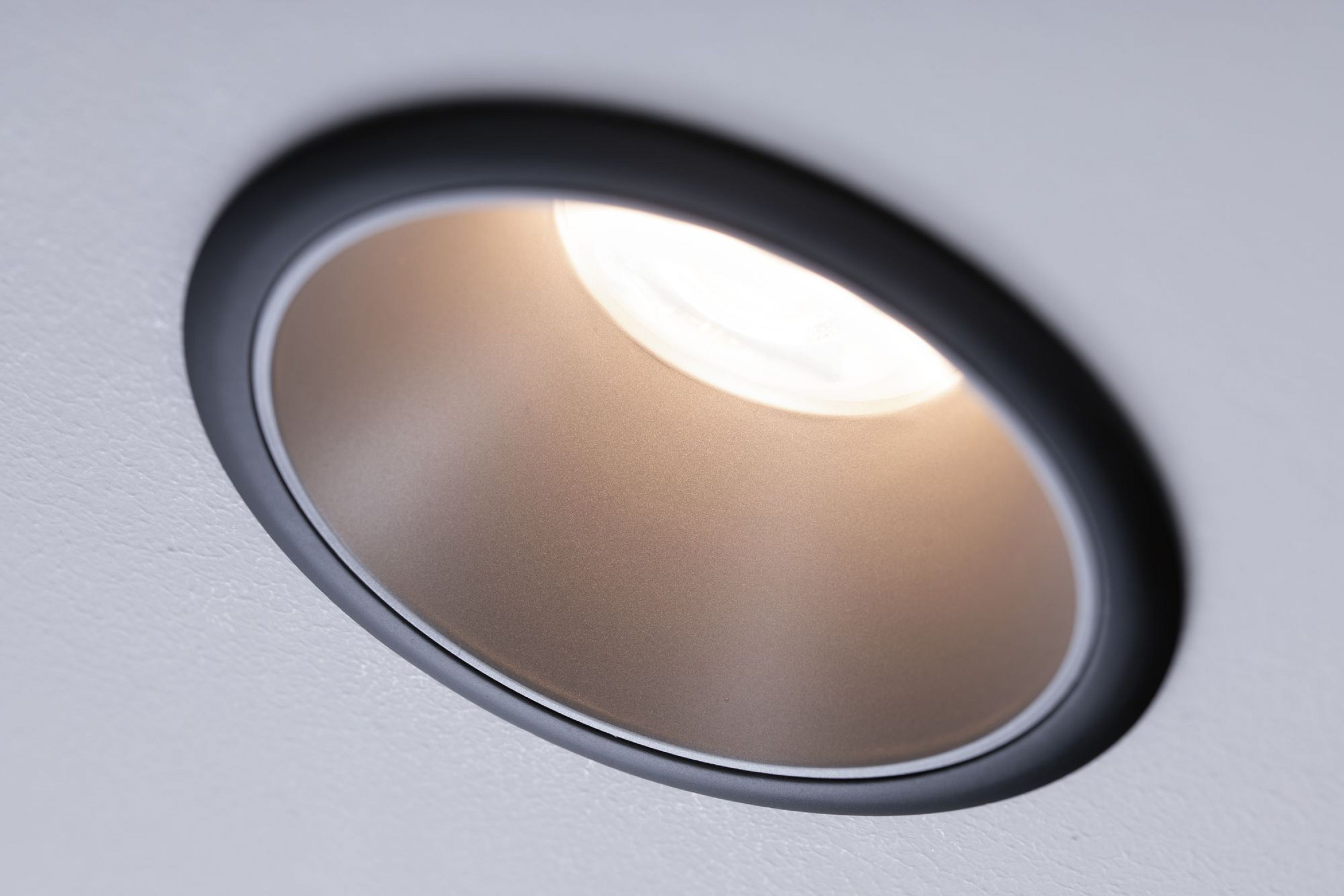 Un apparecchio di illuminazione nero a incasso montato in un soffitto. La luce è accesa.