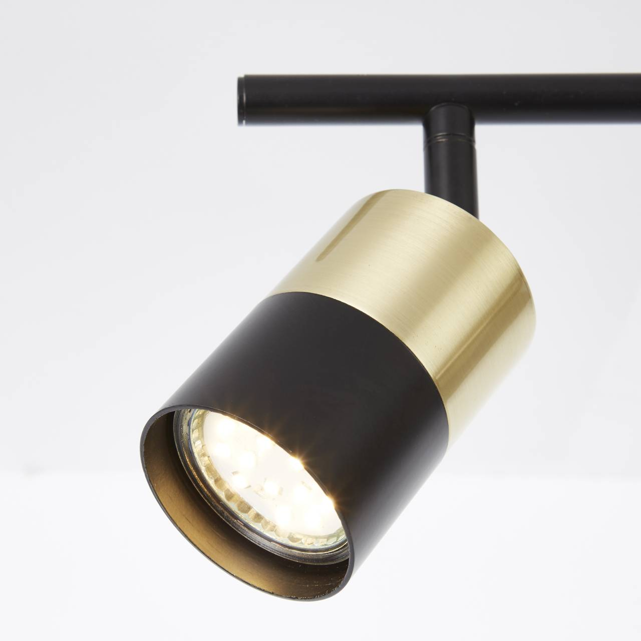 Ein schwarzer Strahler mit goldenem Akzent leuchtet auf weißem Hintergrund.
