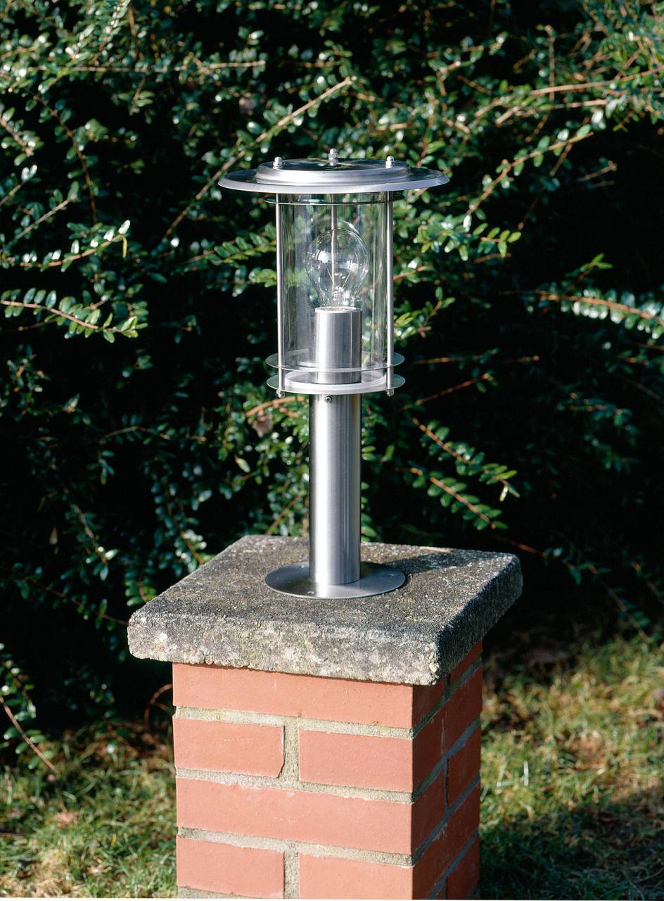 Eine Edelstahl-Gartenleuchte mit Glühbirne auf einem Ziegelsteinsockel.