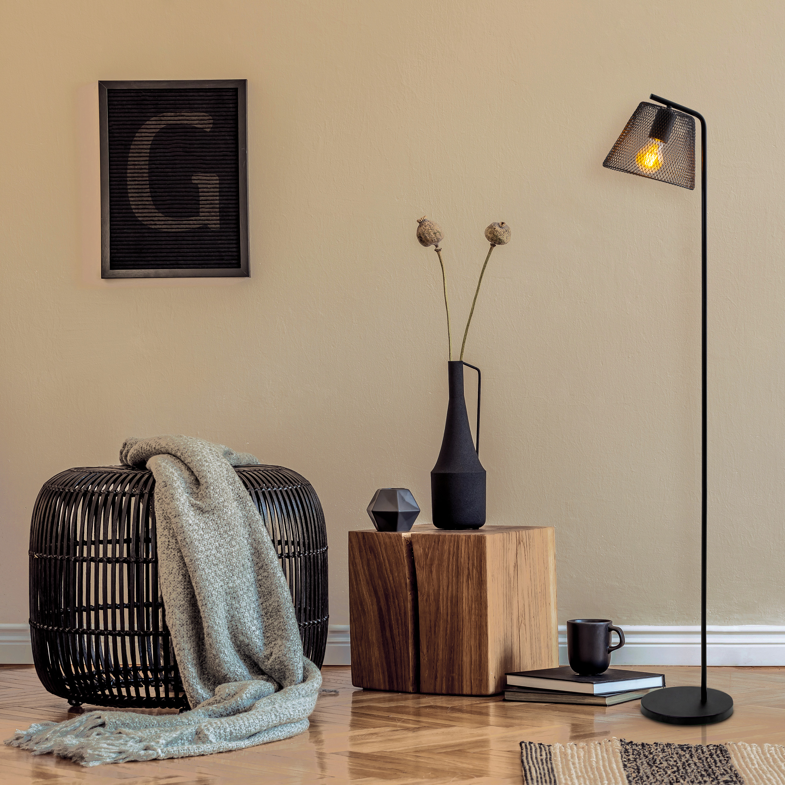 Ein modernes Wohnzimmer mit einer hohen, schwarzen Stehlampe, einem schwarzen Hocker, einem kleinen Holztisch und einem gerahmten Bild.