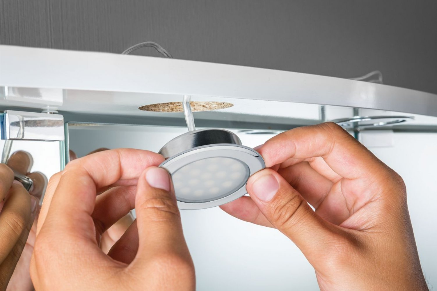 Mani che installano un apparecchio di illuminazione a LED rotondo in un armadio.