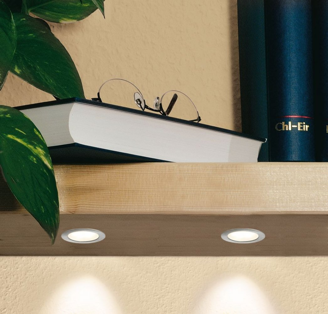 Libri, occhiali e due luci installate su una mensola di legno, sfondo neutro.