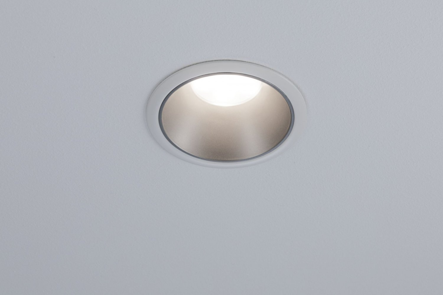 Eine Einbauleuchte in einer weißen Decke. Das Licht ist an, die Umgebung ist weiß.