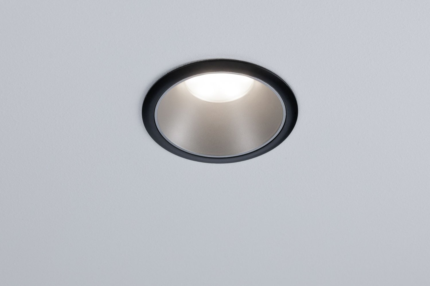 Un faretto da incasso, cornice nera, interno illuminato, su un soffitto bianco.