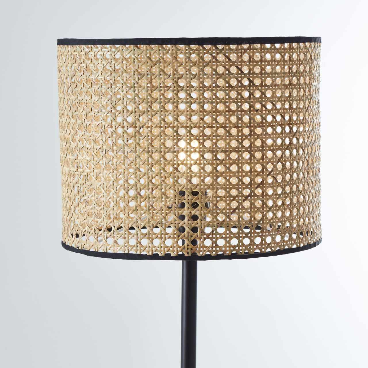Eine Lampe mit einem geflochtenen Schirm aus Rattan und schwarzem Rand.
