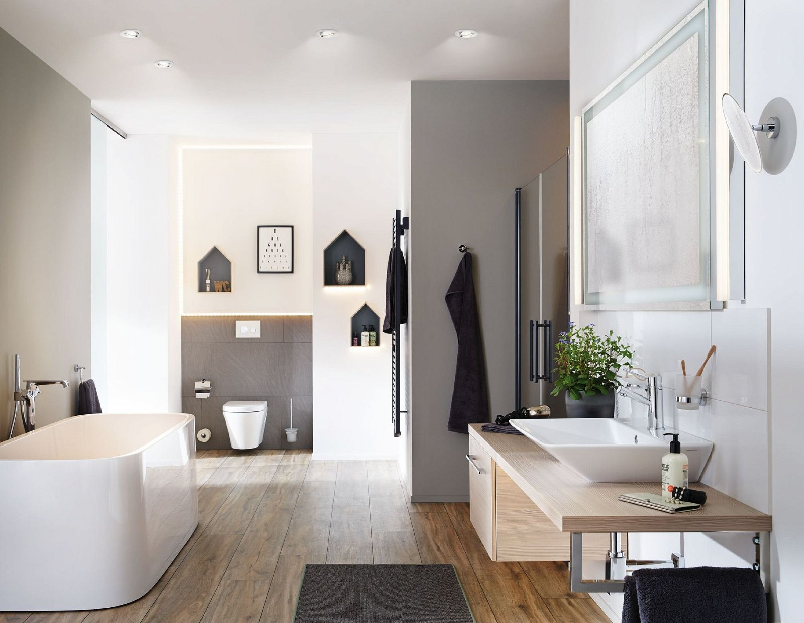 Bagno moderno con vasca da bagno bianca, pavimento in legno e un grande specchio con luce.