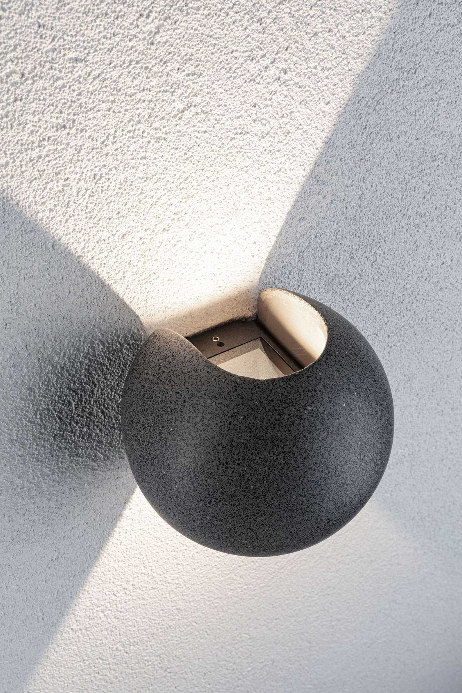 Dunkelgraue Außenwandleuchte. Runde Form, strukturierte Wand, Schatten.