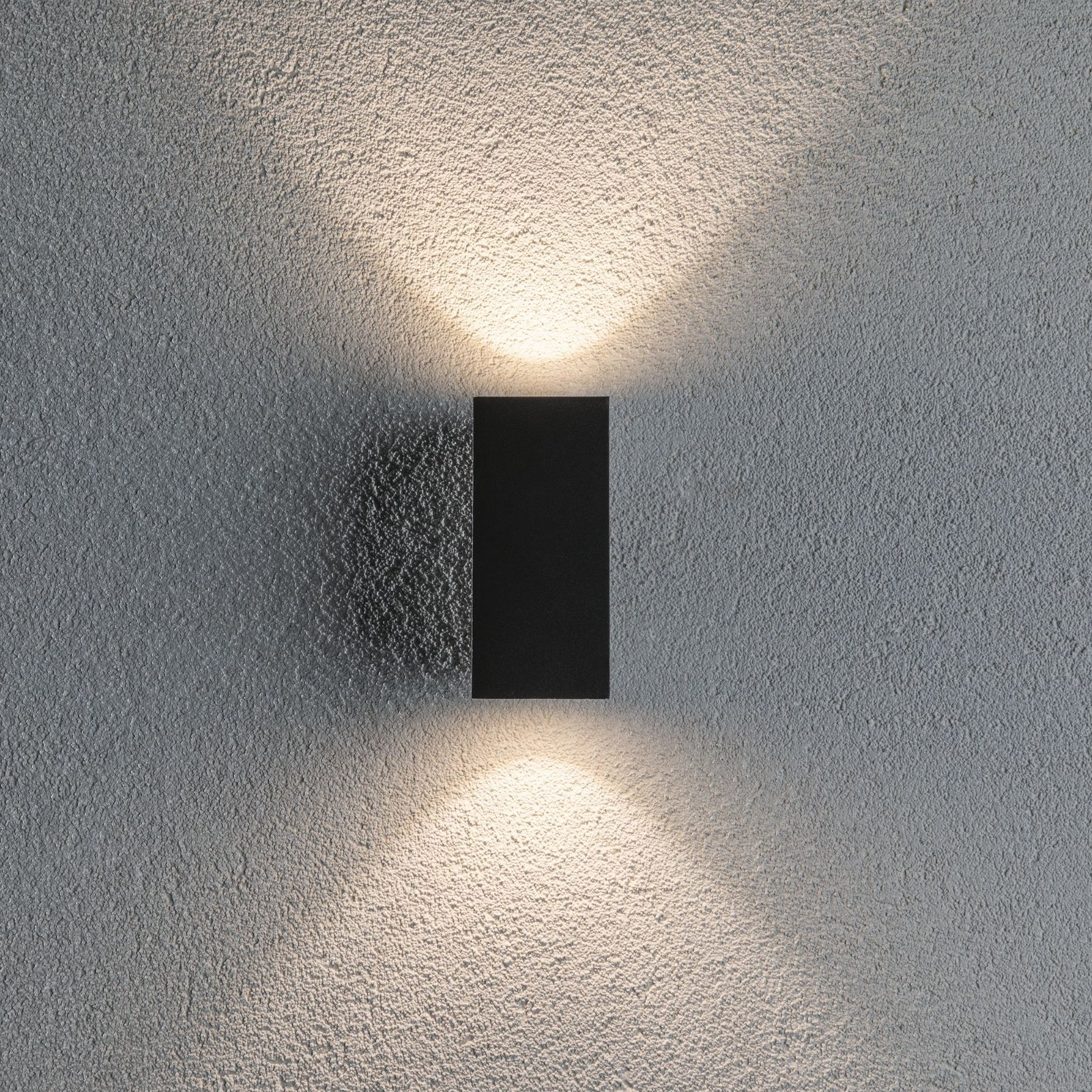 Czarna prostokątna lampa ścienna z dwoma wiązkami światła na teksturowanej szarej ścianie.